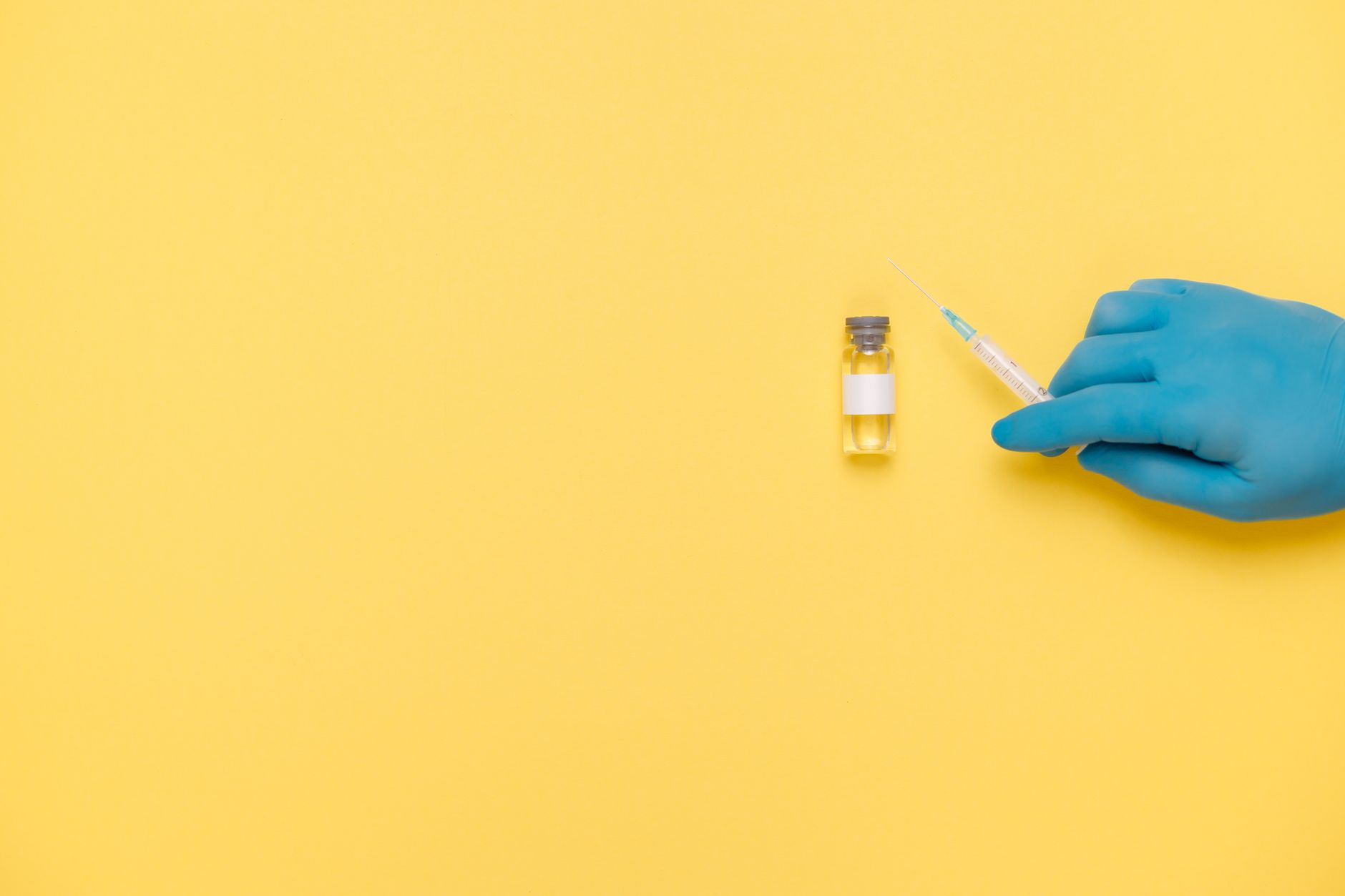 Blue gloved hand holding a syringe near a vaccine vial on a
