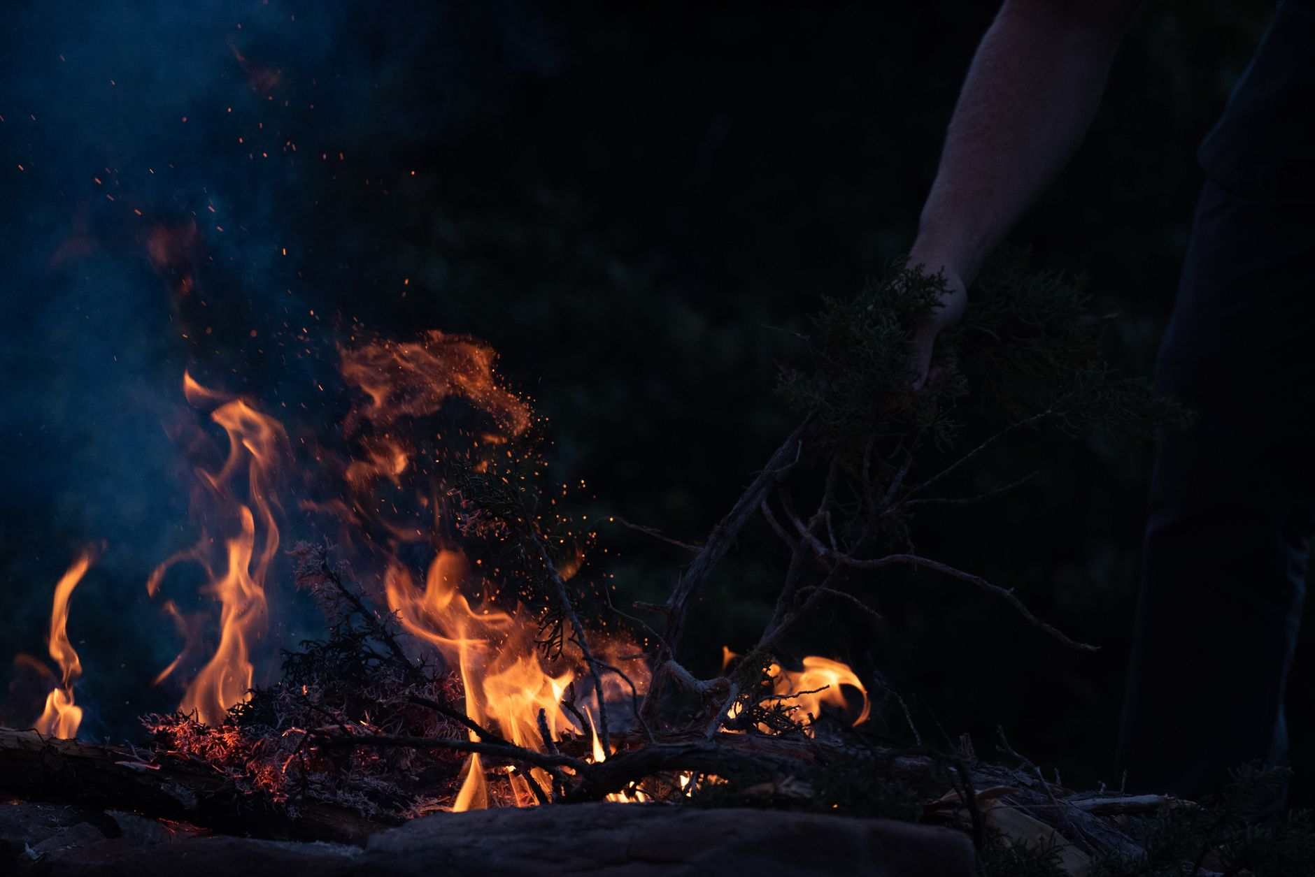 A person tends a vivid campfire in the dark near Zion National
