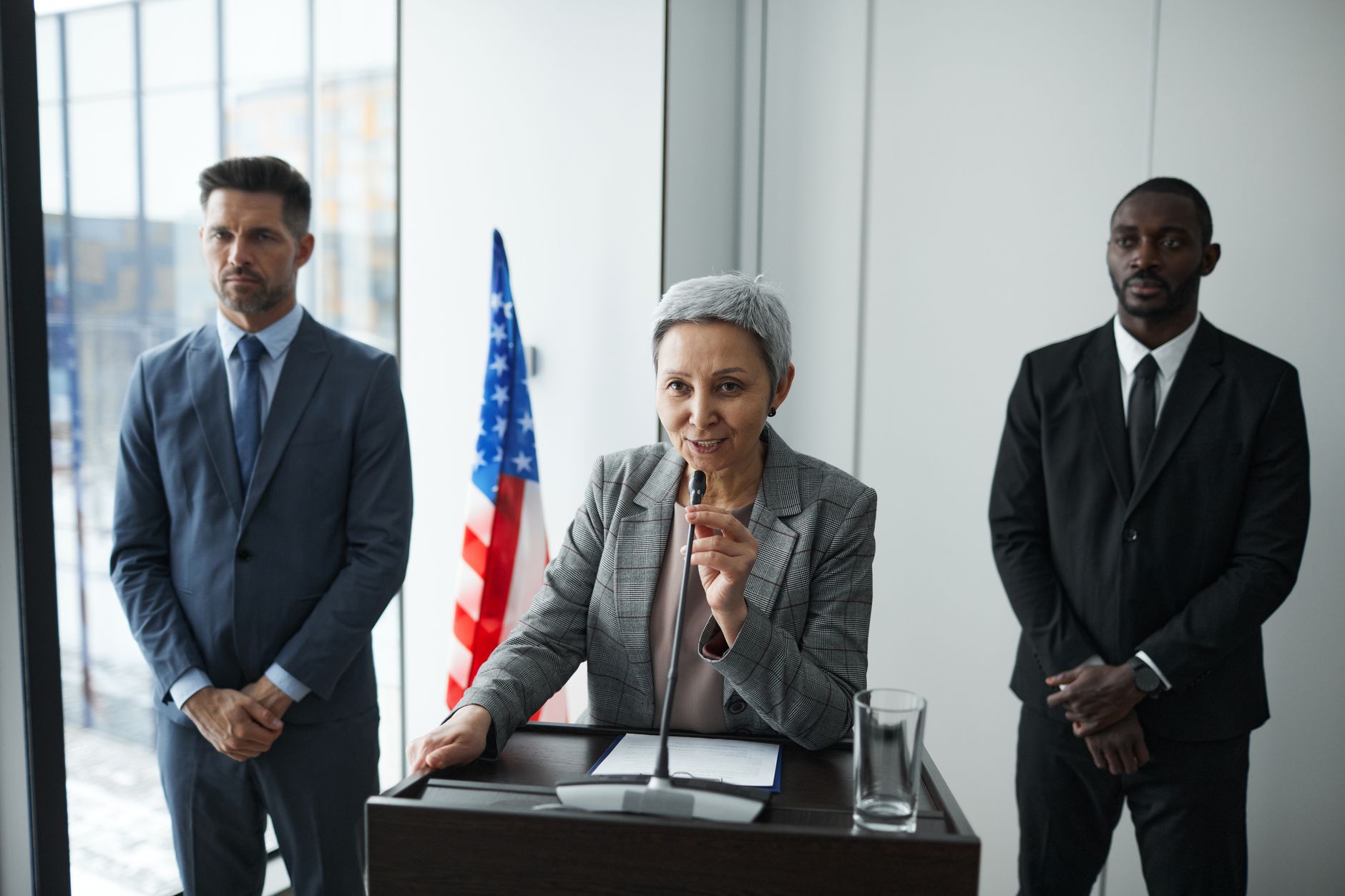 A female politician delivers a speech with bodyguards and an American flag