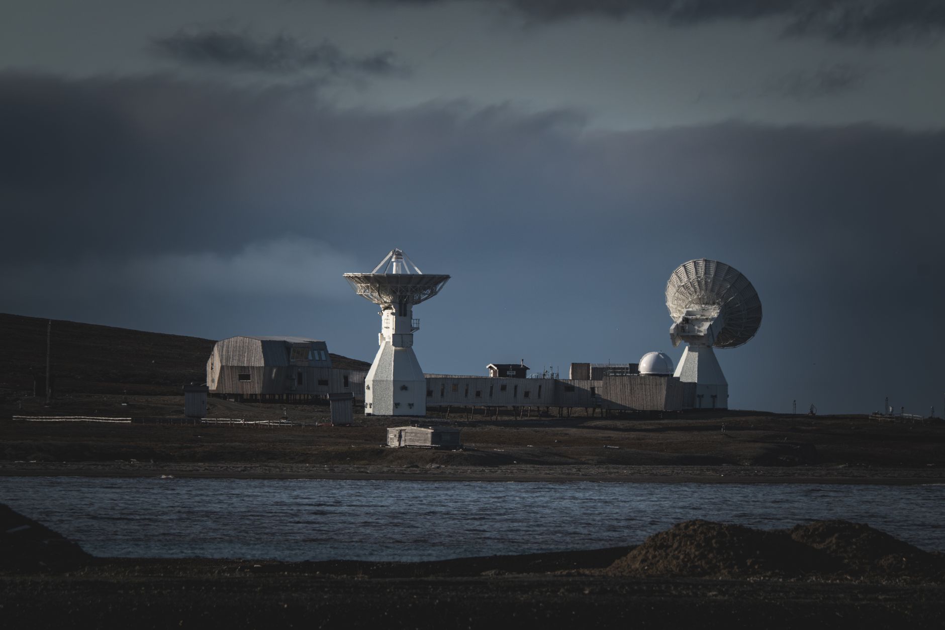 A remote satellite station with large dishes stands under a moody dark