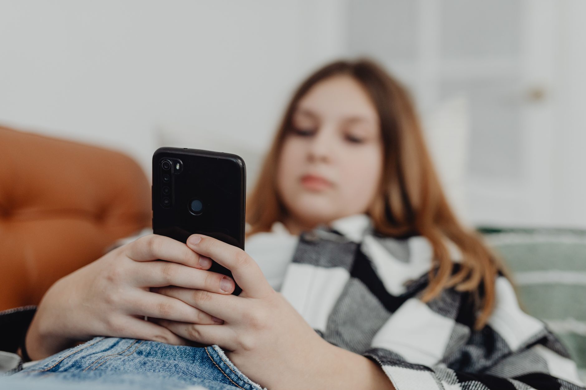 Teenage girl using smartphone while relaxing on a sofa, depicting leisure and