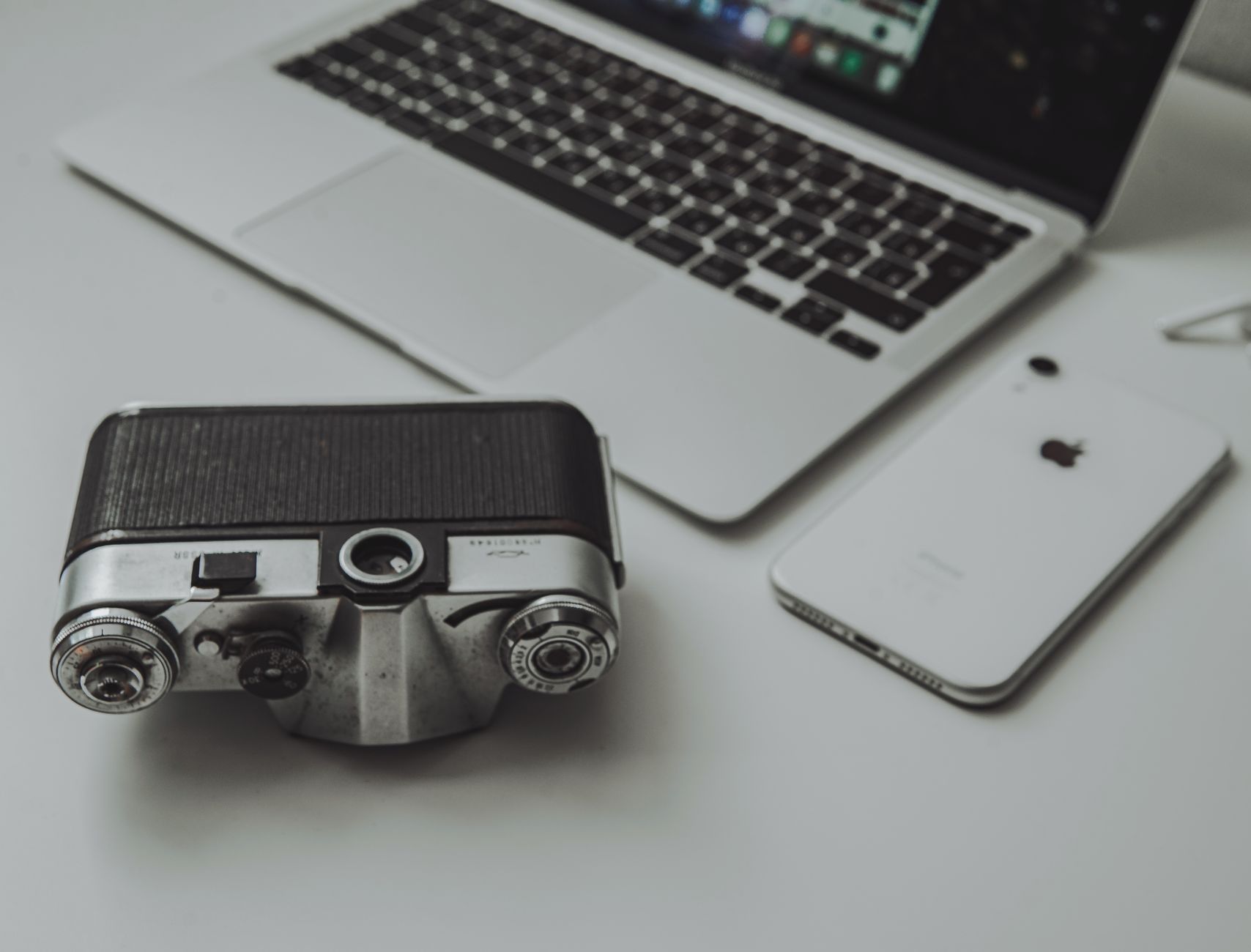 A vintage camera alongside a modern laptop and smartphone, blending old and new tech.