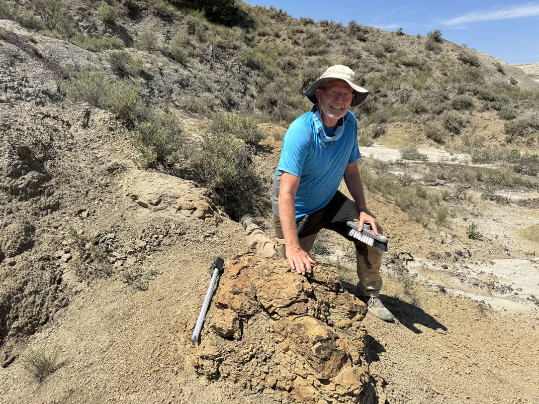 A man in a blue shirt posing next to a rock
