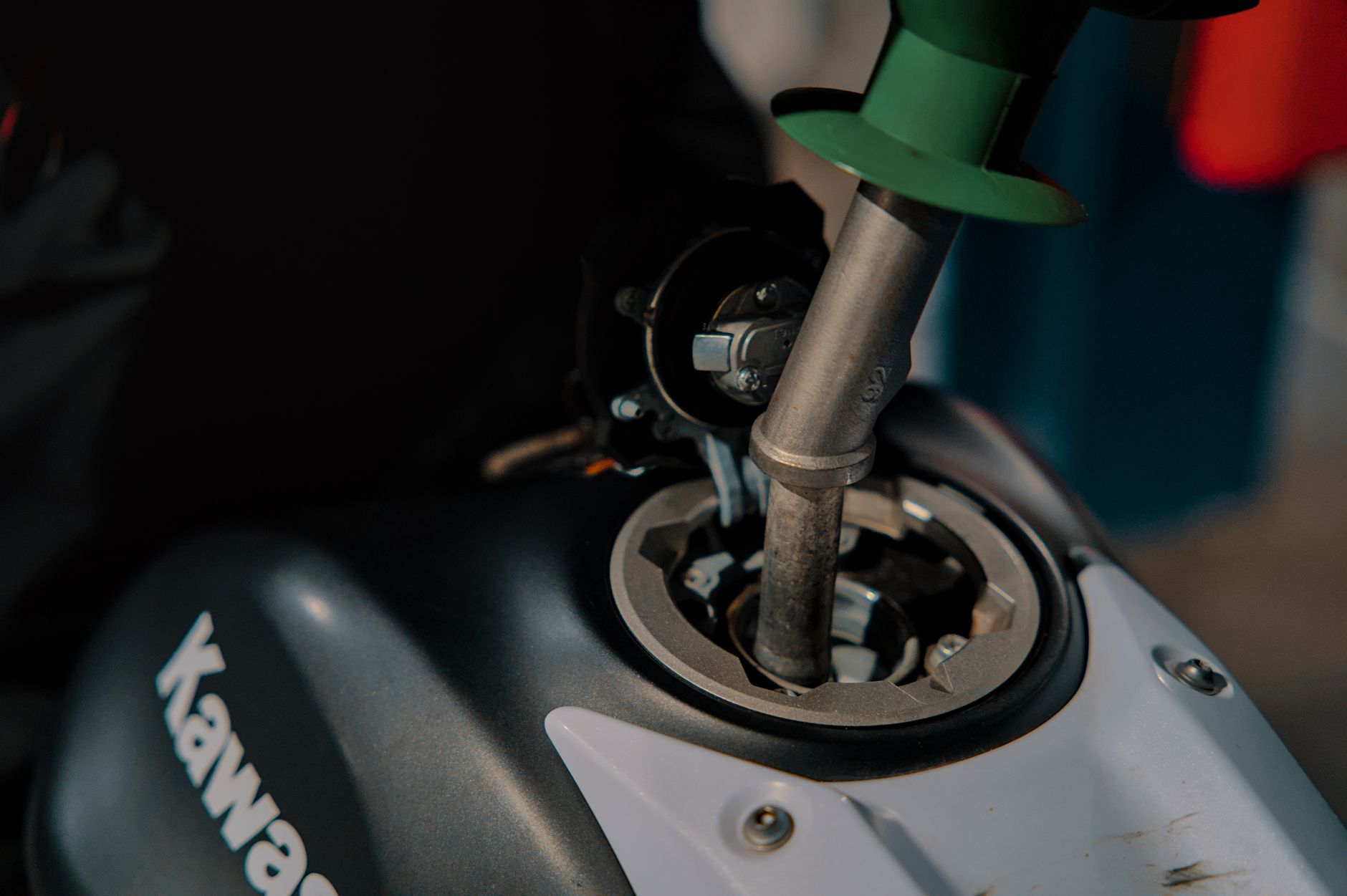 Close-up of refueling a Kawasaki motorcycle at a gas station, with nozzle