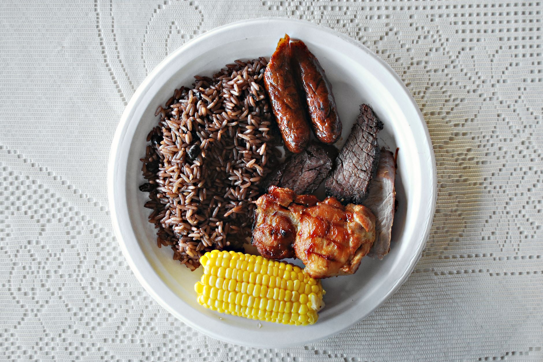A delicious barbecue plate featuring rice, grilled meats, and corn on a