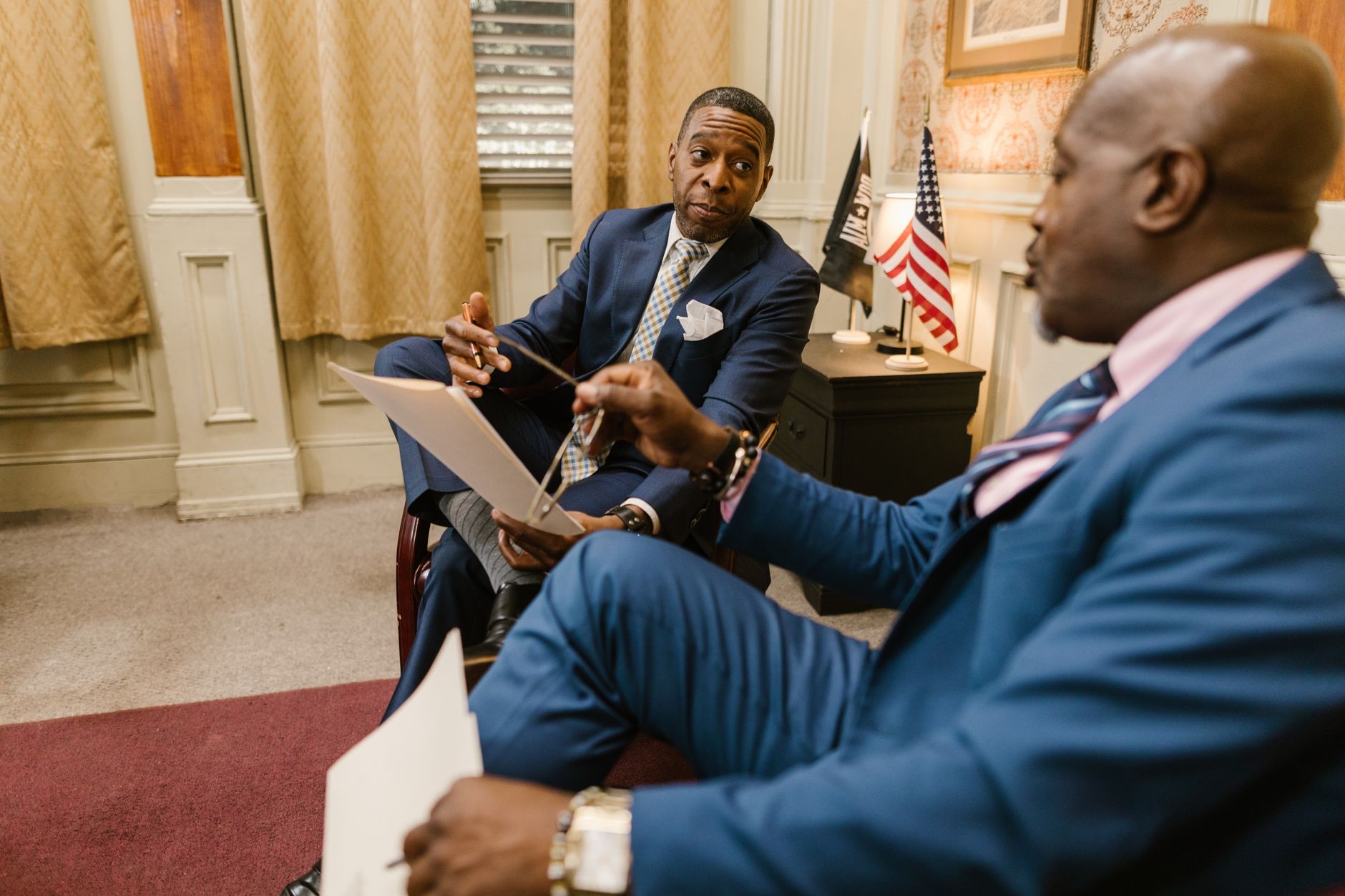 Two business professionals having a conversation indoors with flags in the background.