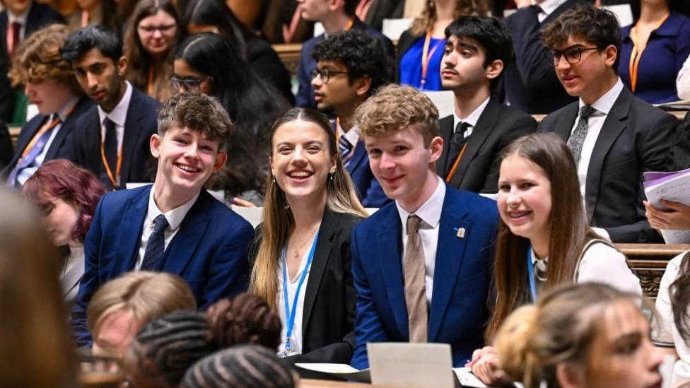 Members of Youth Parliament smile while sat on the benches of the