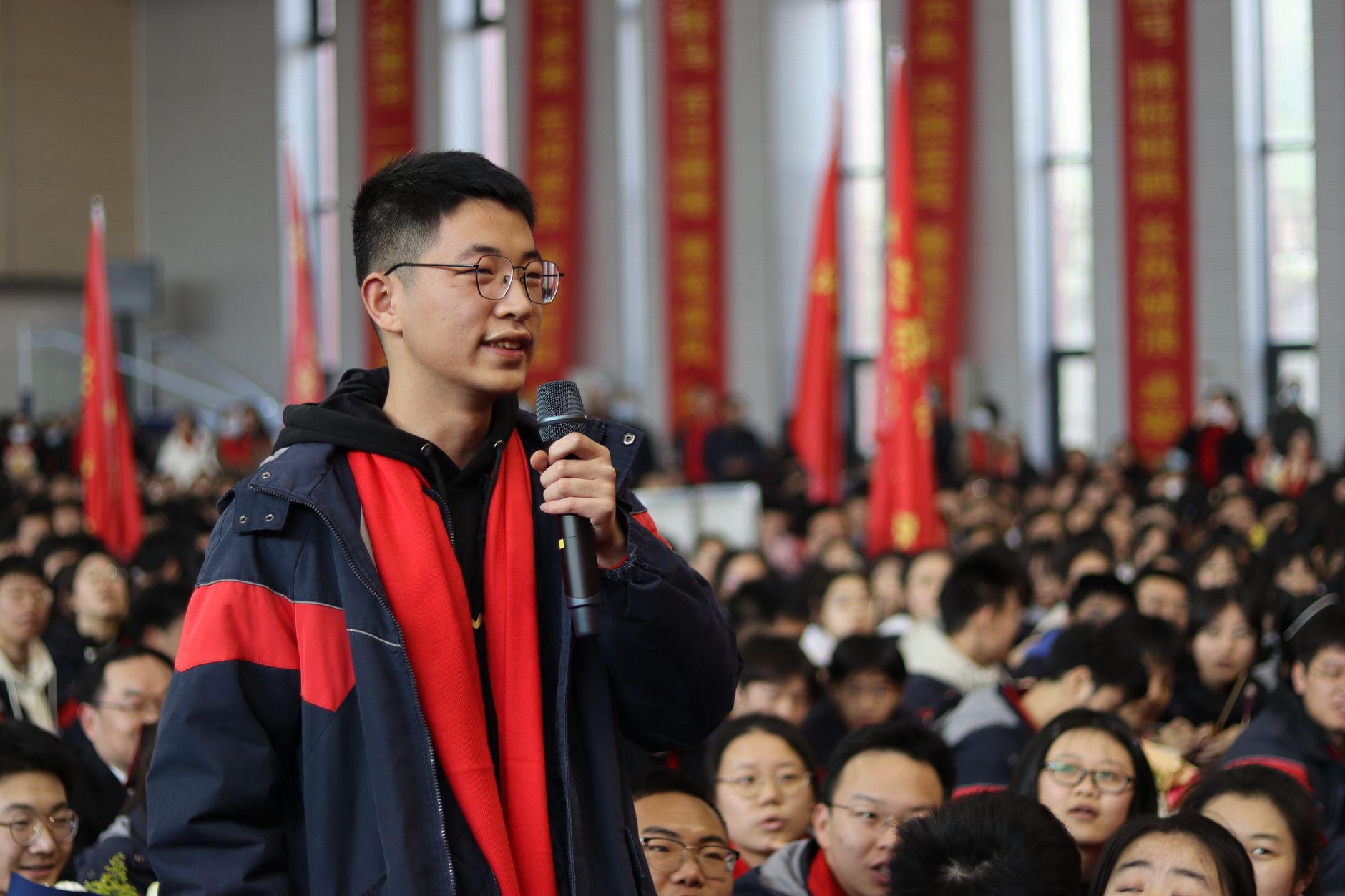 A young man speaking at a crowded indoor event, symbolizing public engagement.