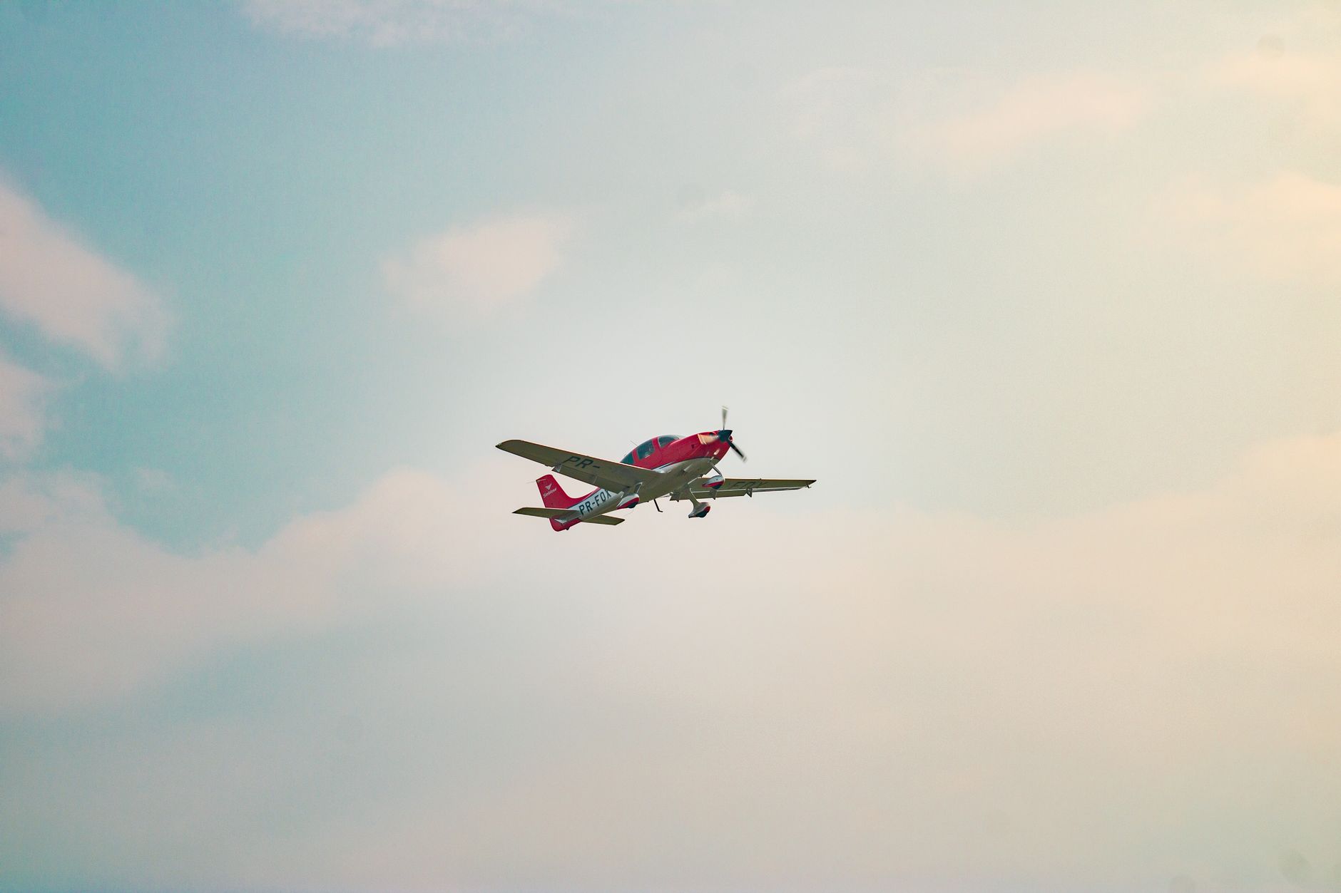 A single-engine red airplane flies smoothly through a clear sky, showcasing aerial