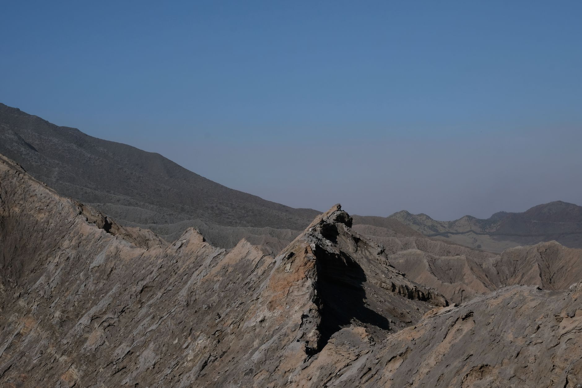 A barren mountain range against a clear, blue sky, showcasing rugged peaks