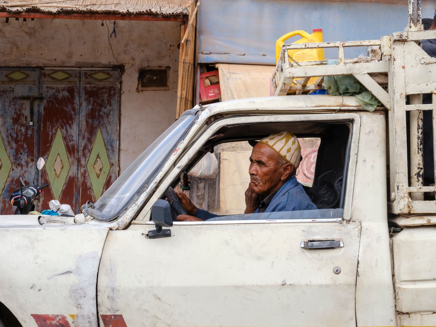 An elderly man drives a vintage pickup truck through a bustling street