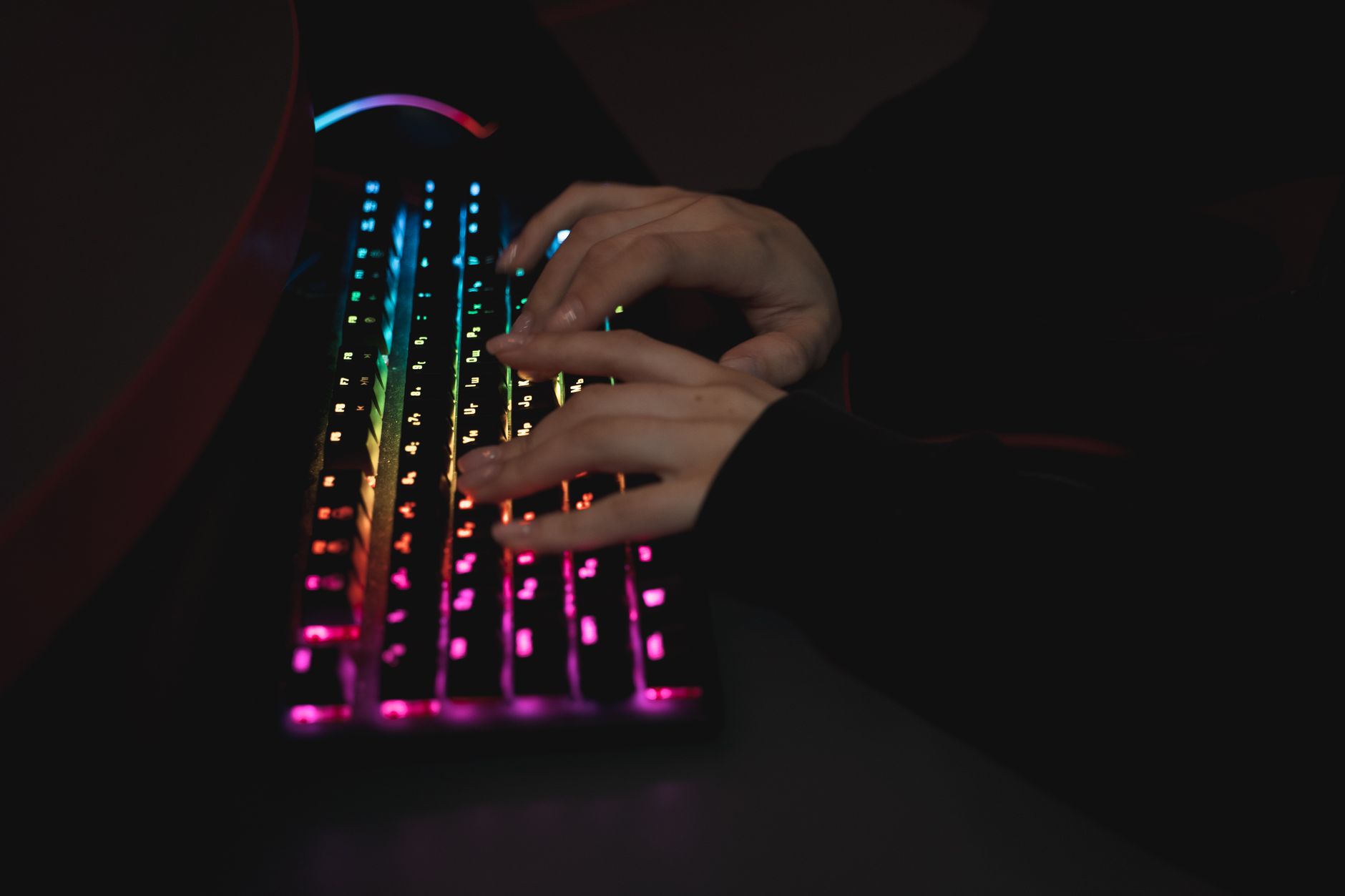 Close-up of hands typing on a colorful RGB backlit mechanical keyboard in