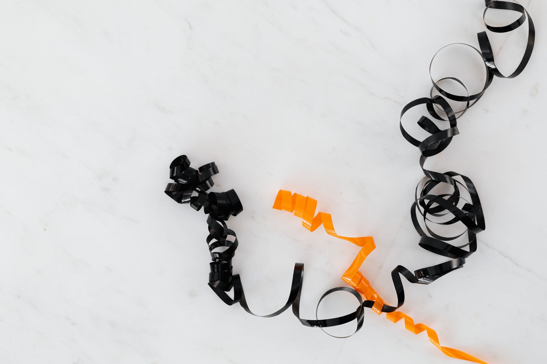 Stylish black and orange curling ribbons on a white marble surface, perfect