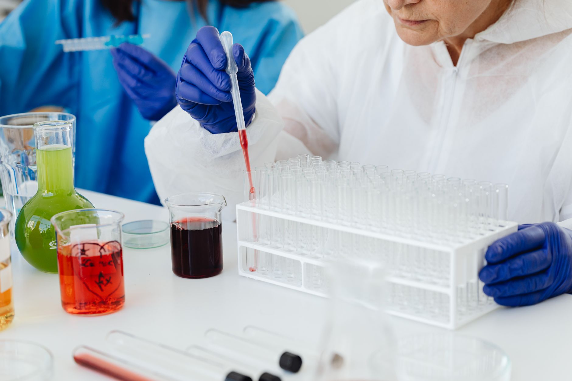 Female scientist in lab coat using pipette on test tubes, focusing on