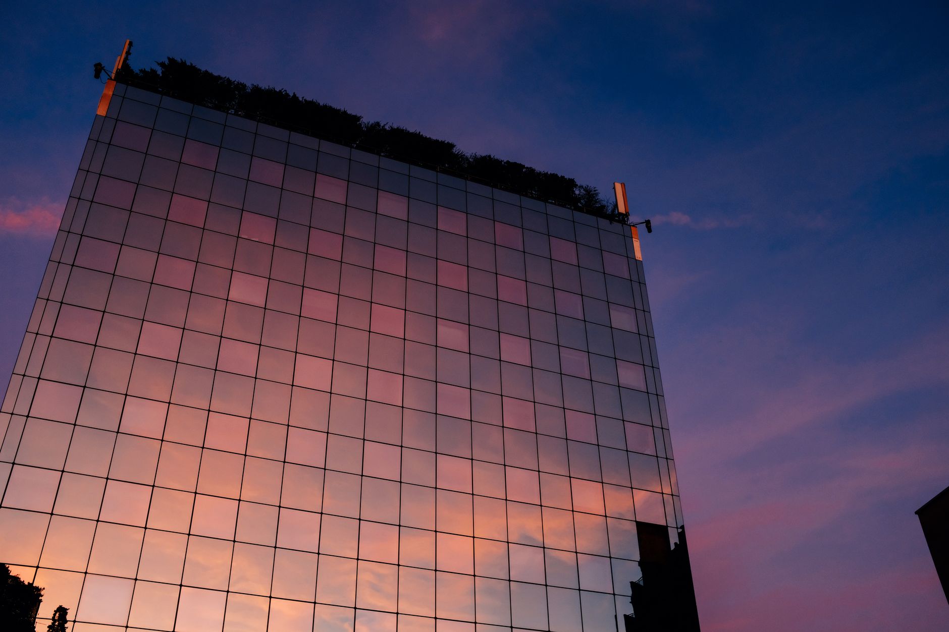 A modern skyscraper with glass facade reflecting a vibrant sunset sky.