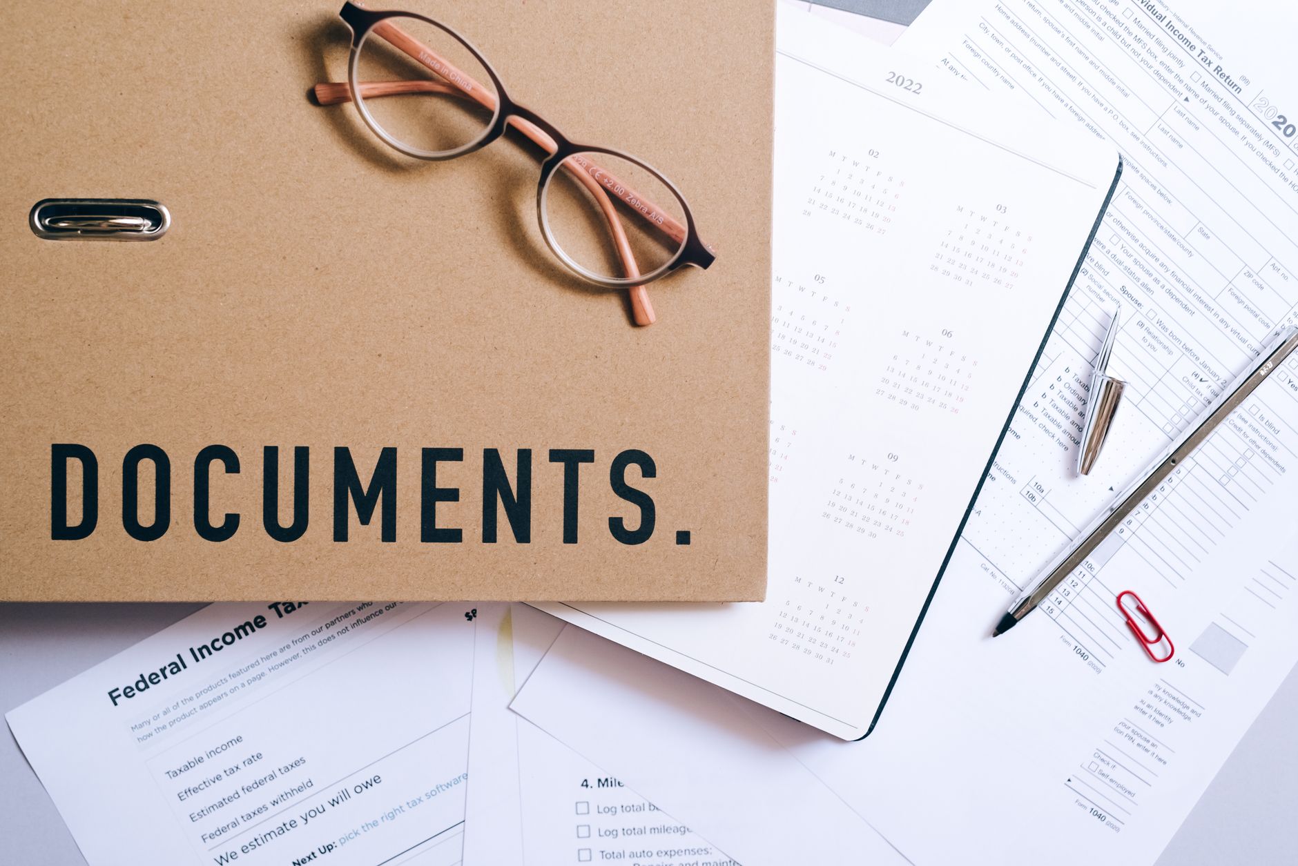 Flat lay of office supplies including documents, calendar, and eyeglasses on a