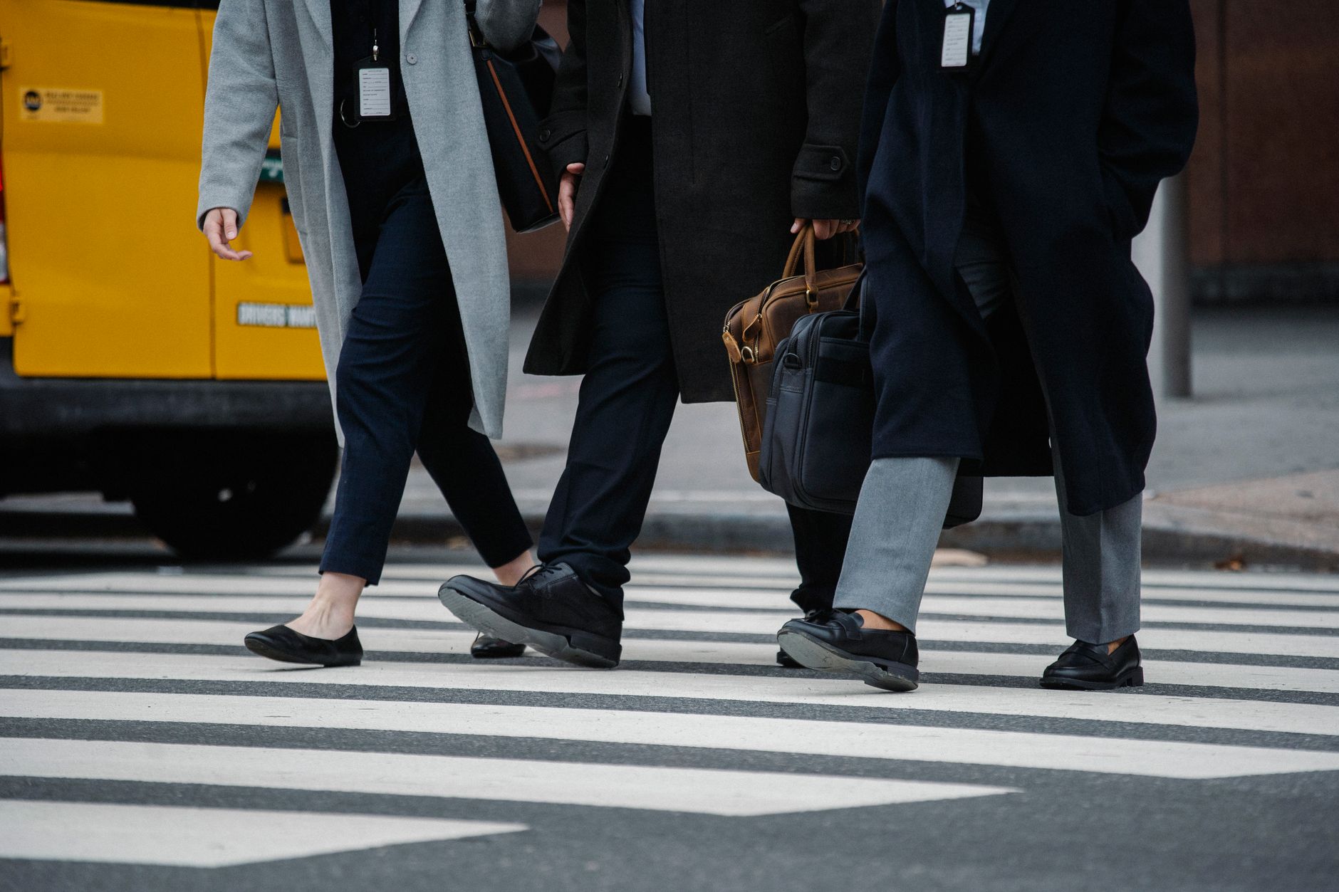 Crop unrecognizable coworkers wearing formal outfits walking together on crosswalk in downtown on autumn day