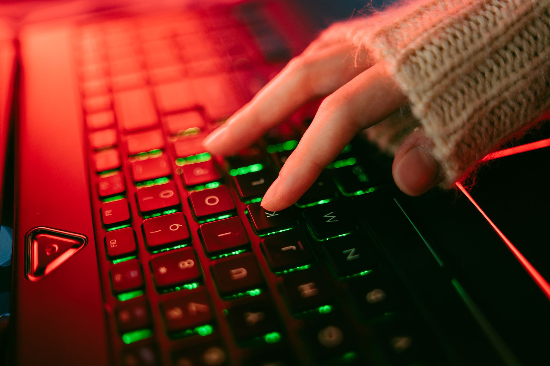 A hand typing on a backlit keyboard in a dark ambiance, highlighting