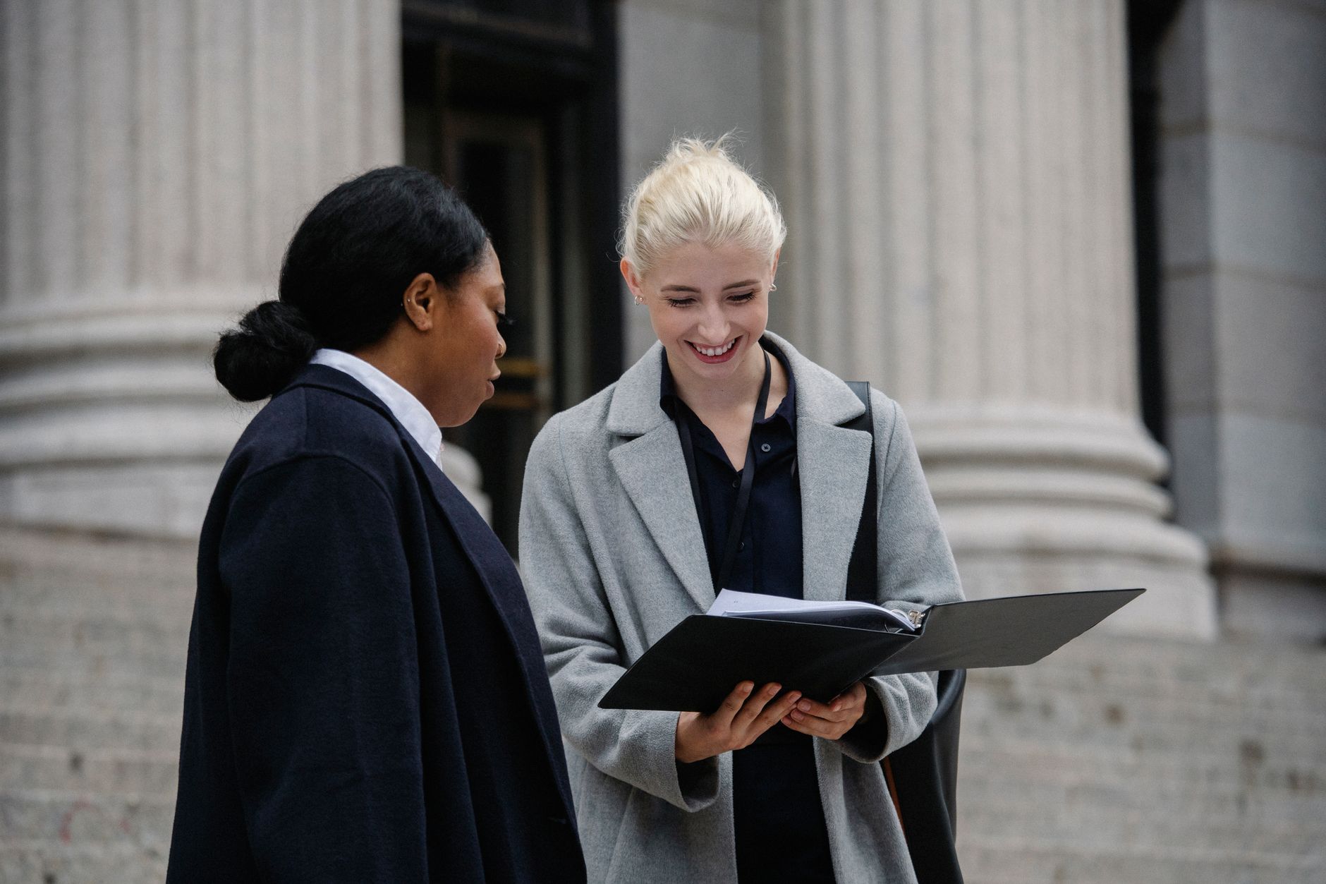Smiling multiracial female coworkers wearing trendy formal outfits standing outside stone building