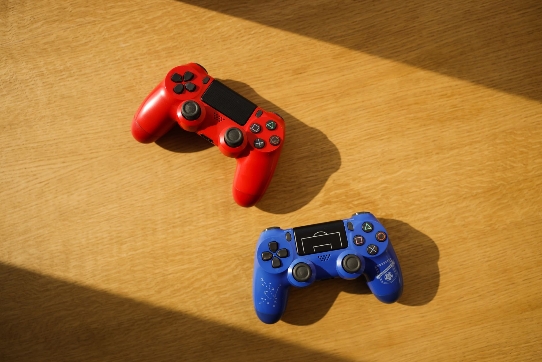 Two colorful gaming controllers placed on a wooden surface with sunlight casting