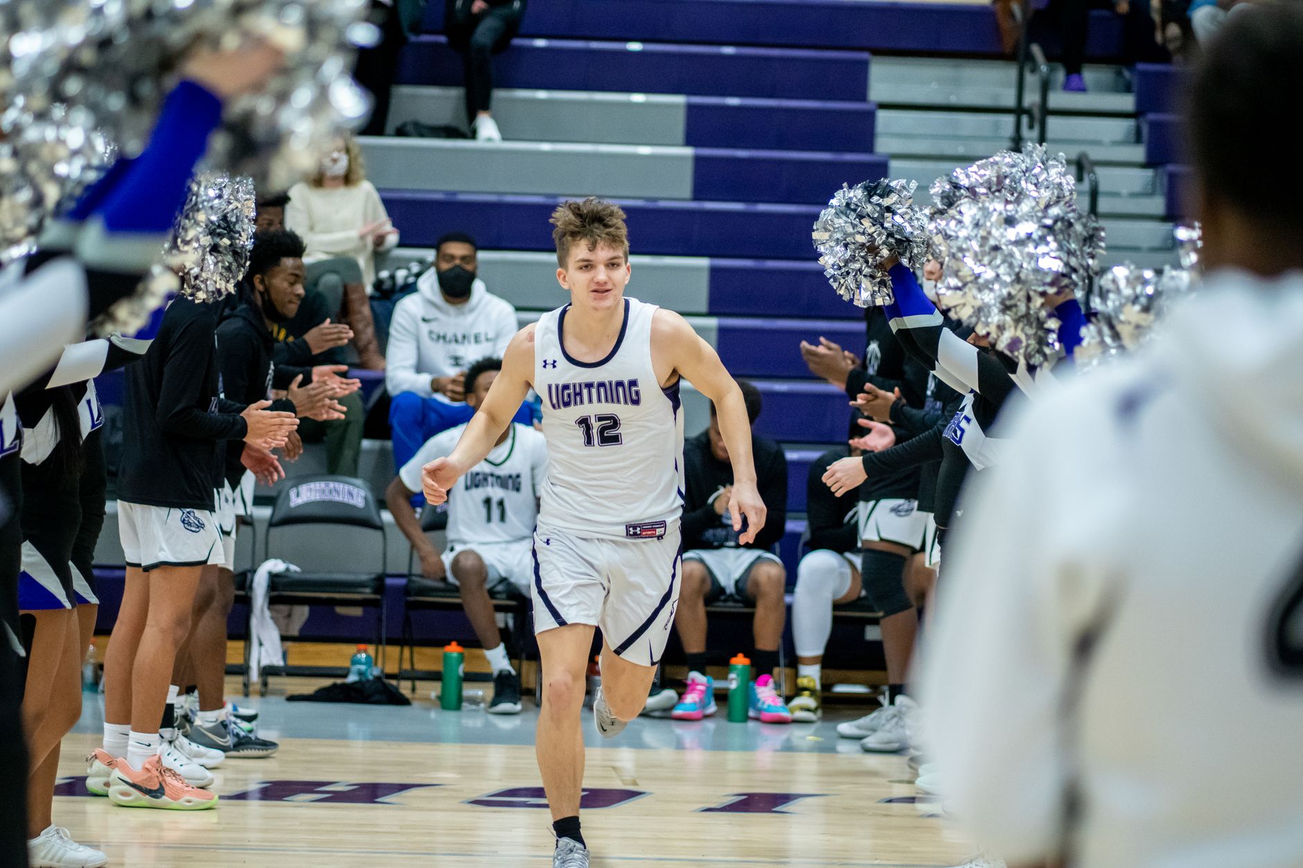 Young basketball player enters court surrounded by cheering teammates and fans.
