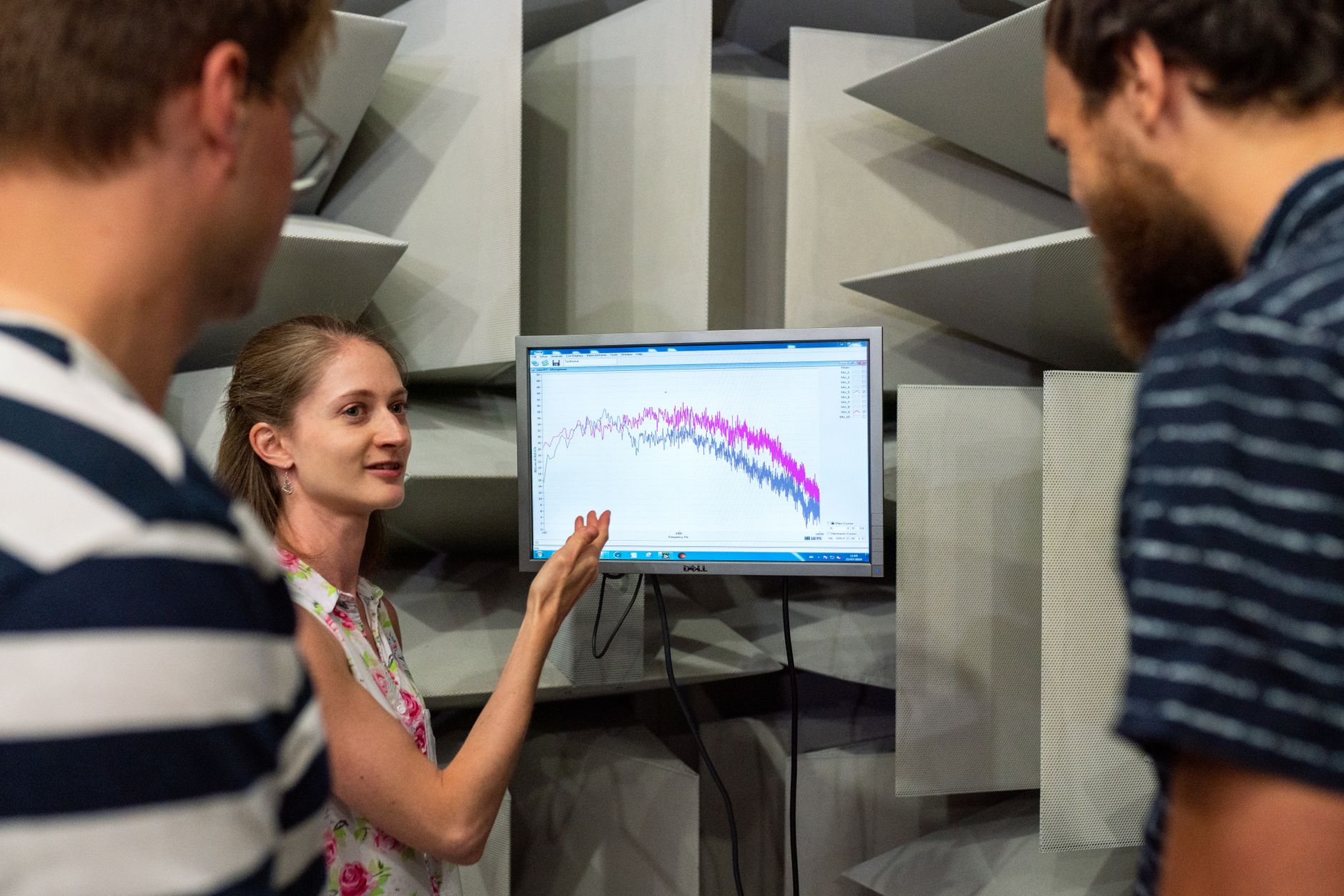 Three engineers discussing sound waves displayed on a monitor in a professional