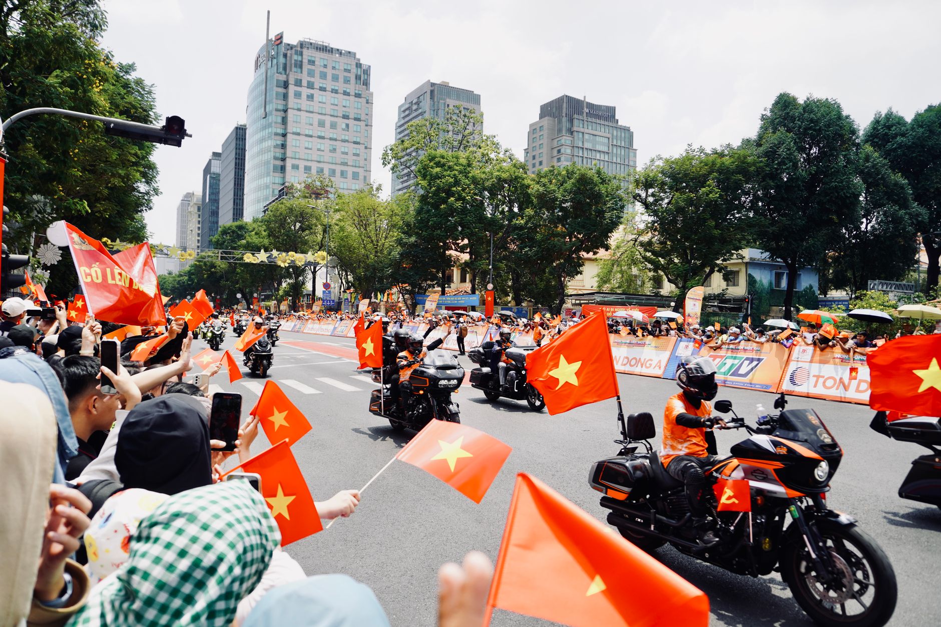 A vibrant motorcycle parade in Vietnam with crowds waving flags and city