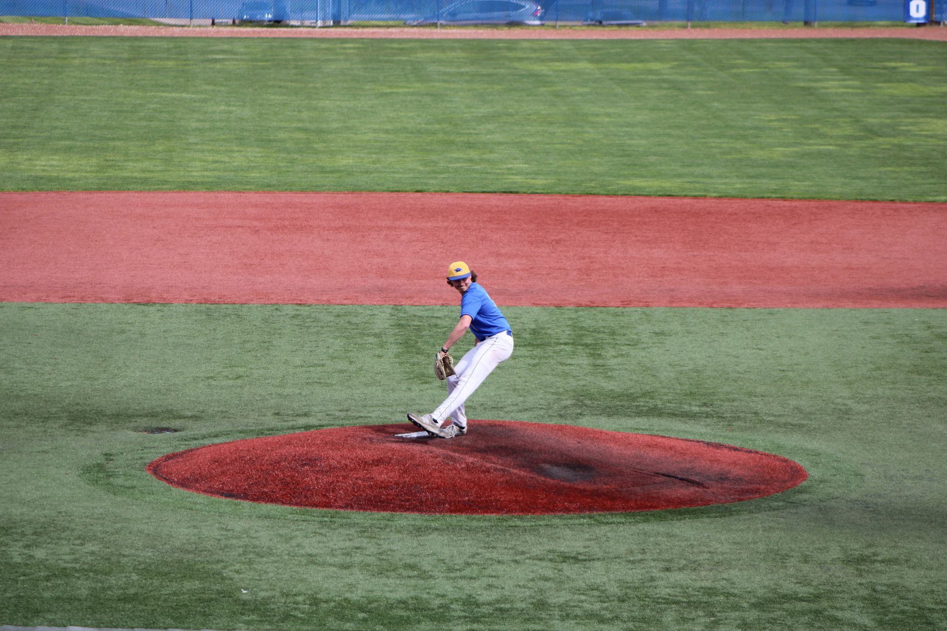 Teenage baseball pitcher throws a ball on an outdoor field, showcasing athletic