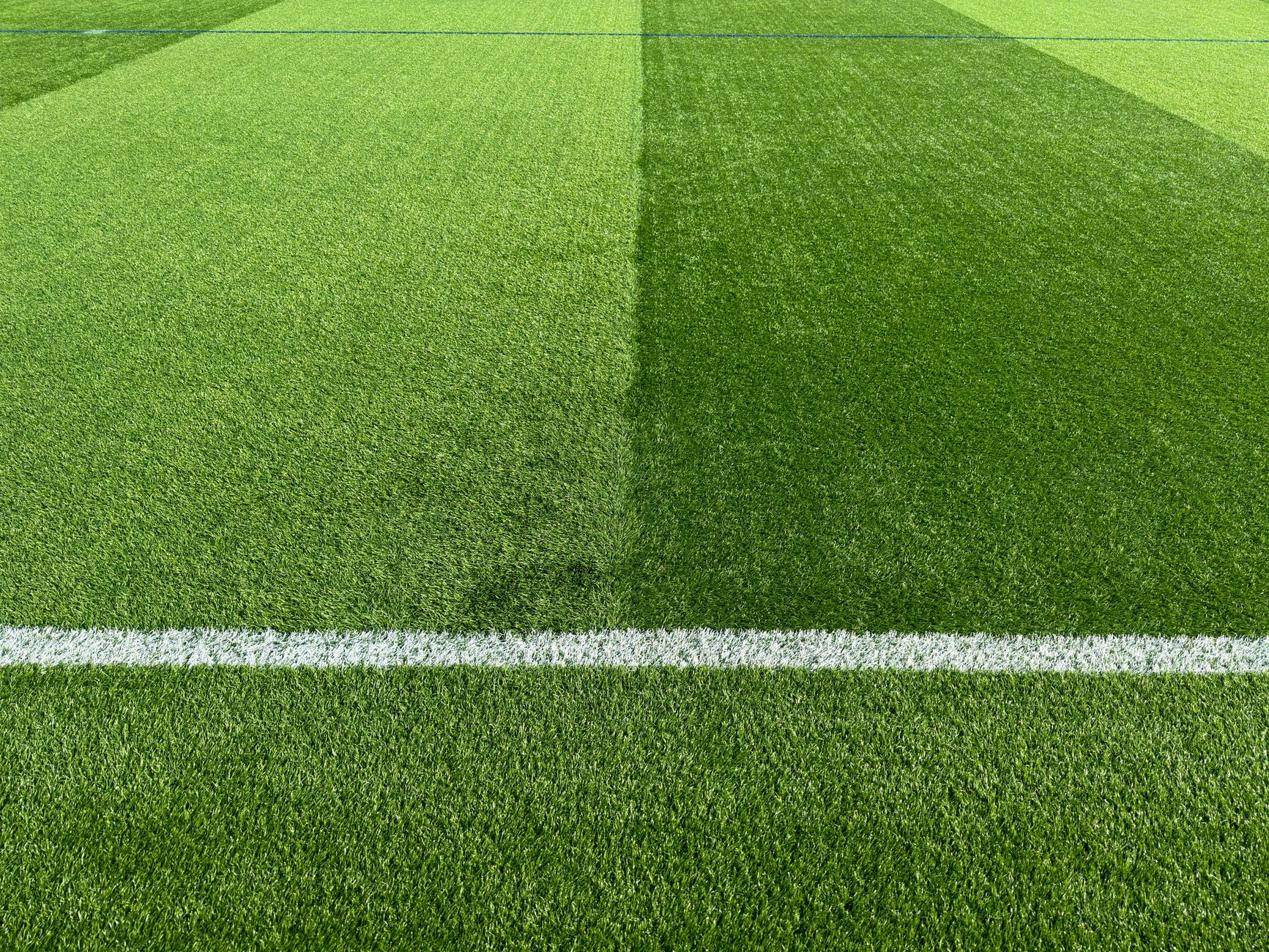 Close-up of a vibrant green football field with a white line marking,