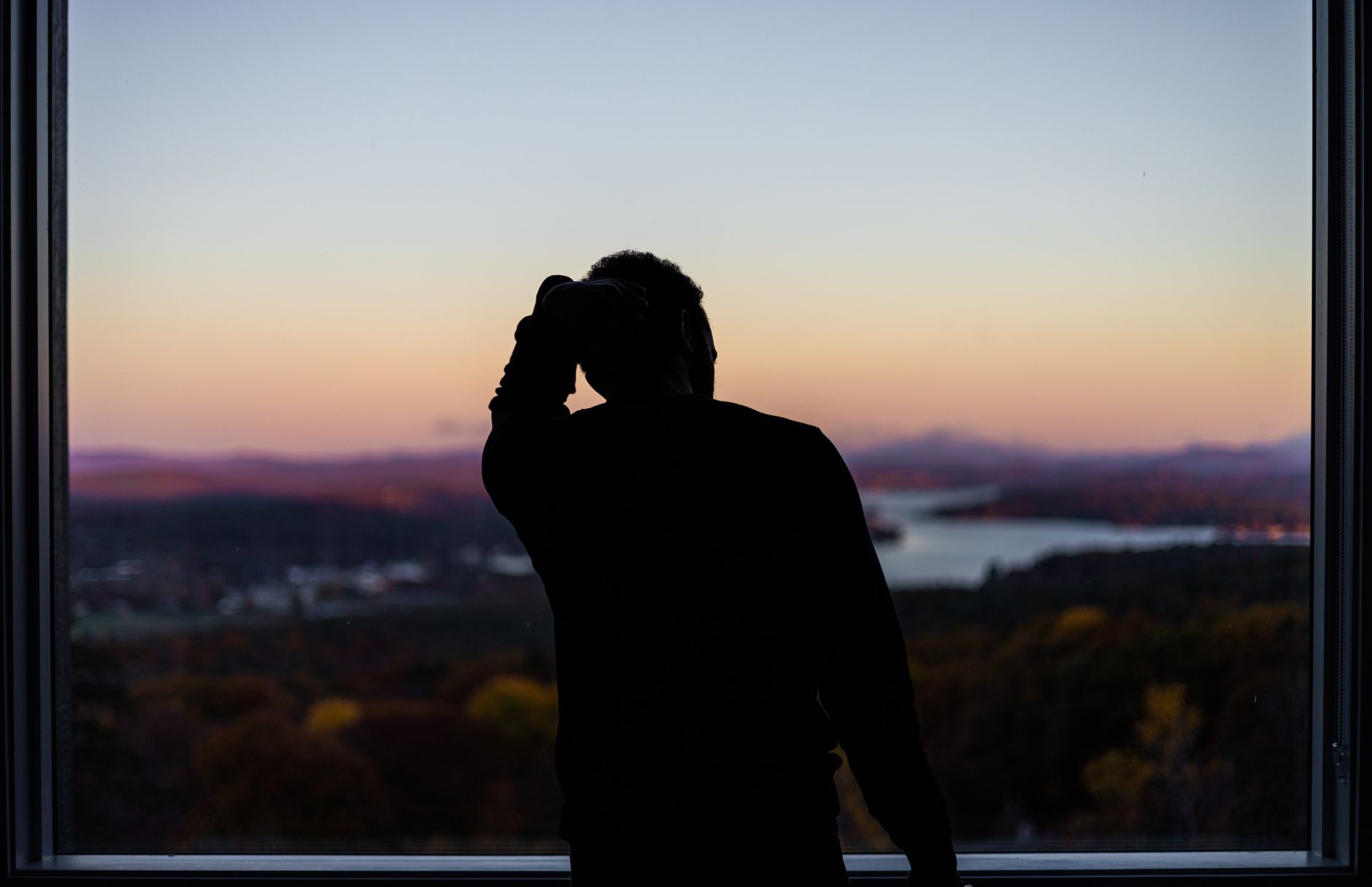A silhouette of a person at a window, gazing at a scenic