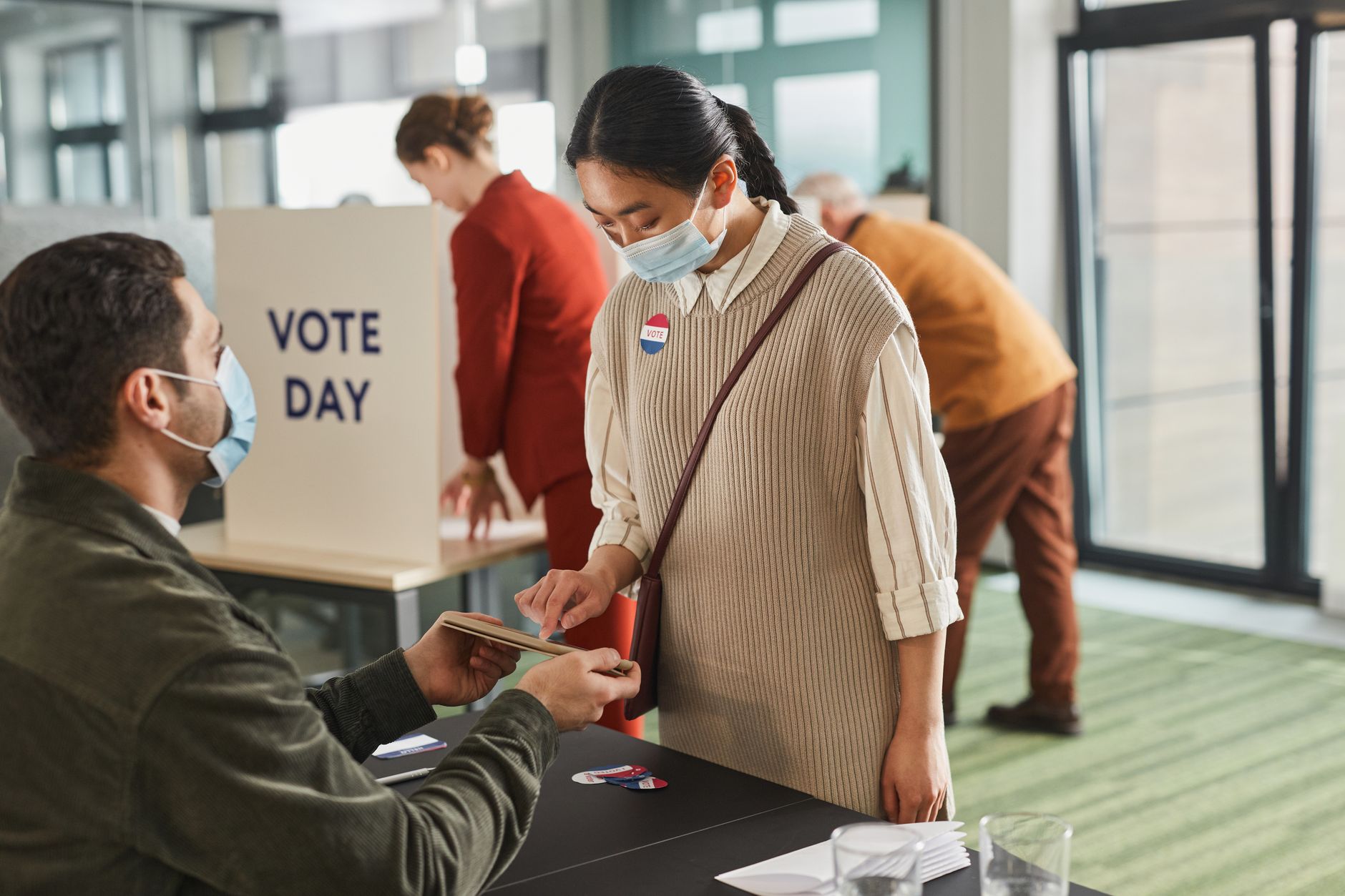 Voters casting ballots indoors on Election Day, wearing masks and using tablets