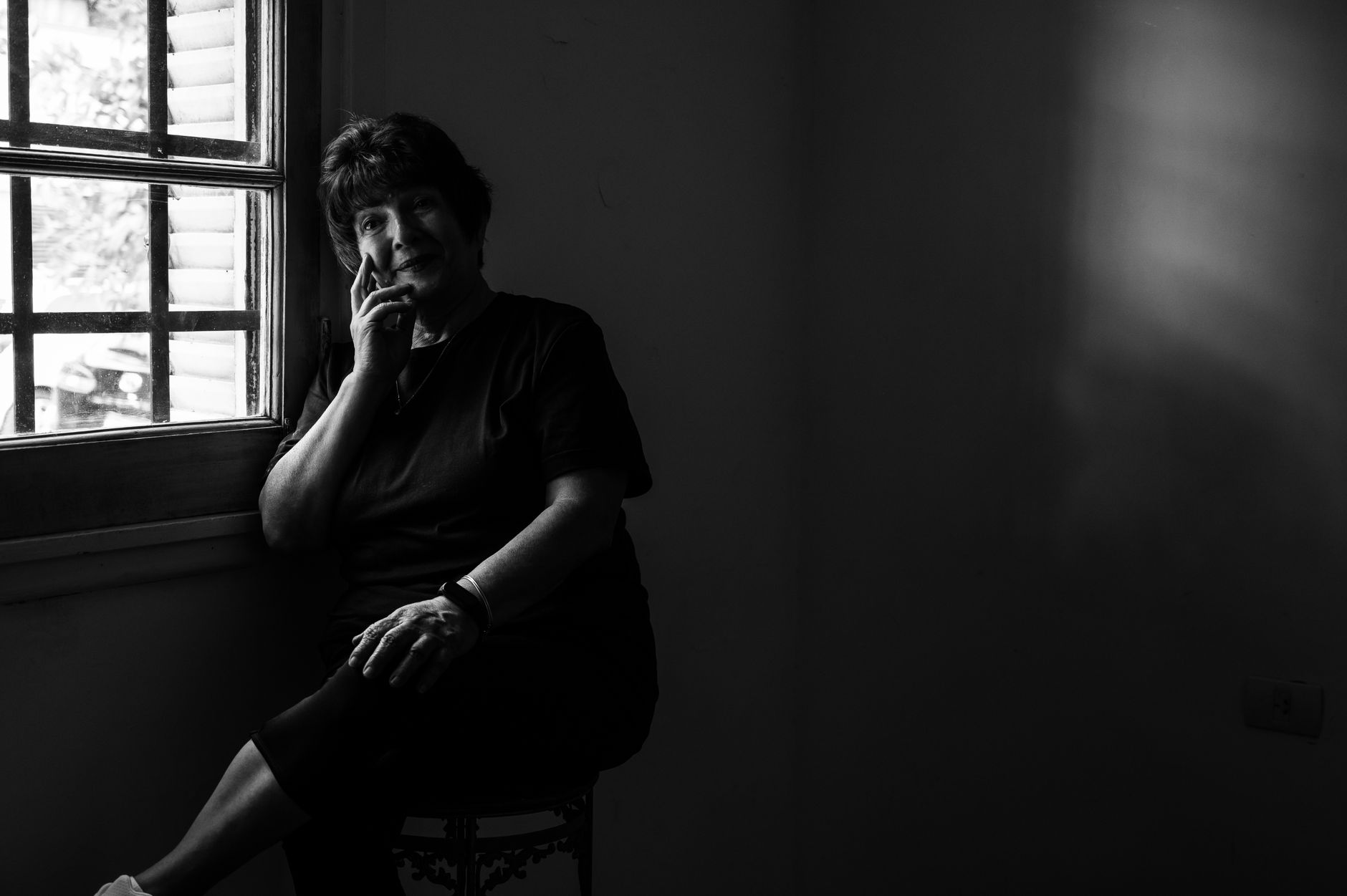 A senior woman sitting thoughtfully by a window in black and white.