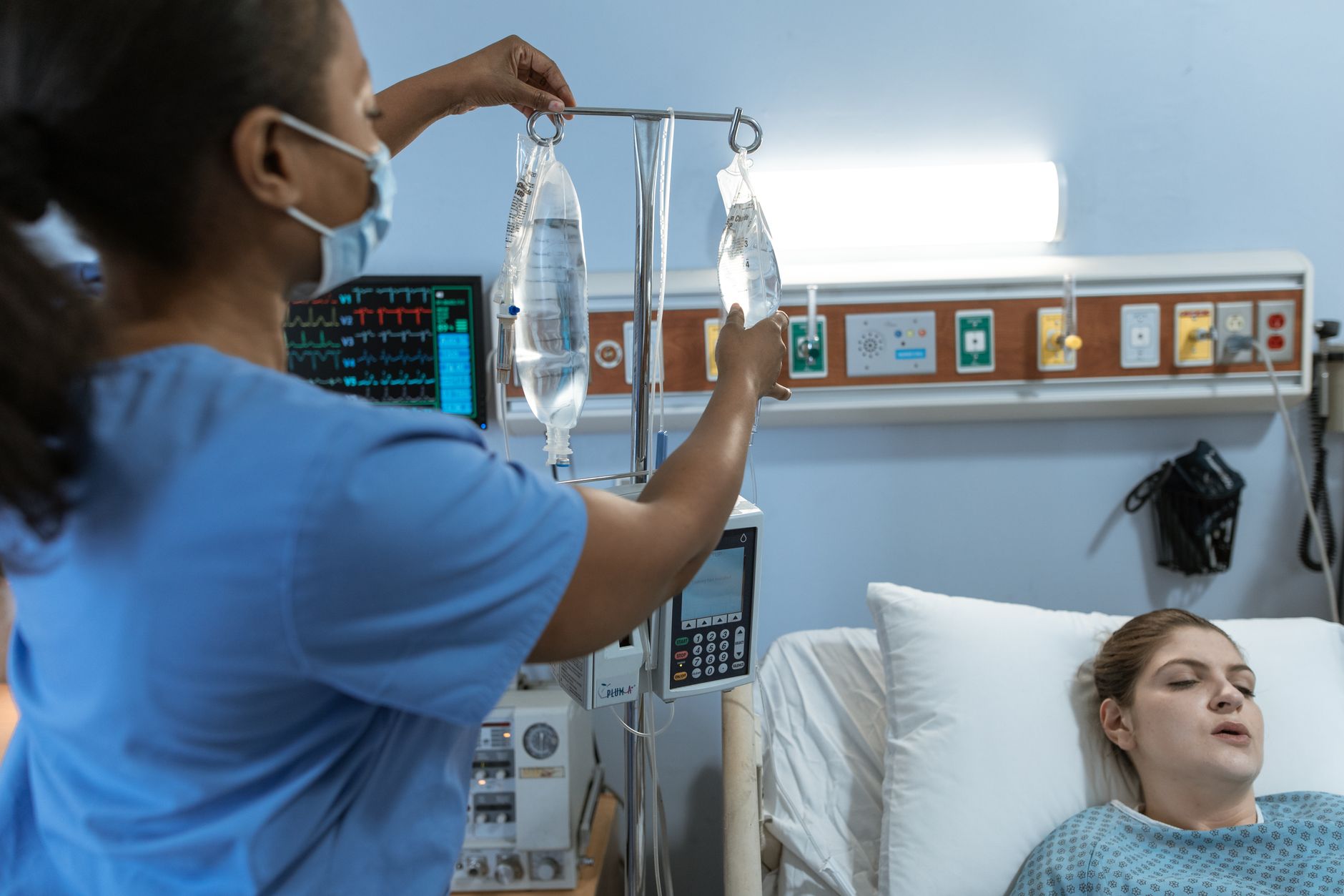 A nurse in a hospital setting adjusts an IV drip for a