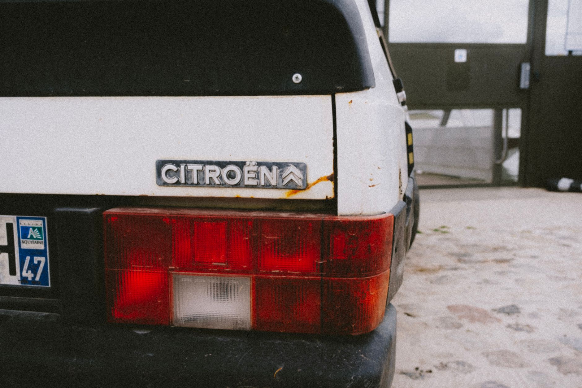 Close-up of a classic Citroën car with a rusty tail light, parked outdoors.