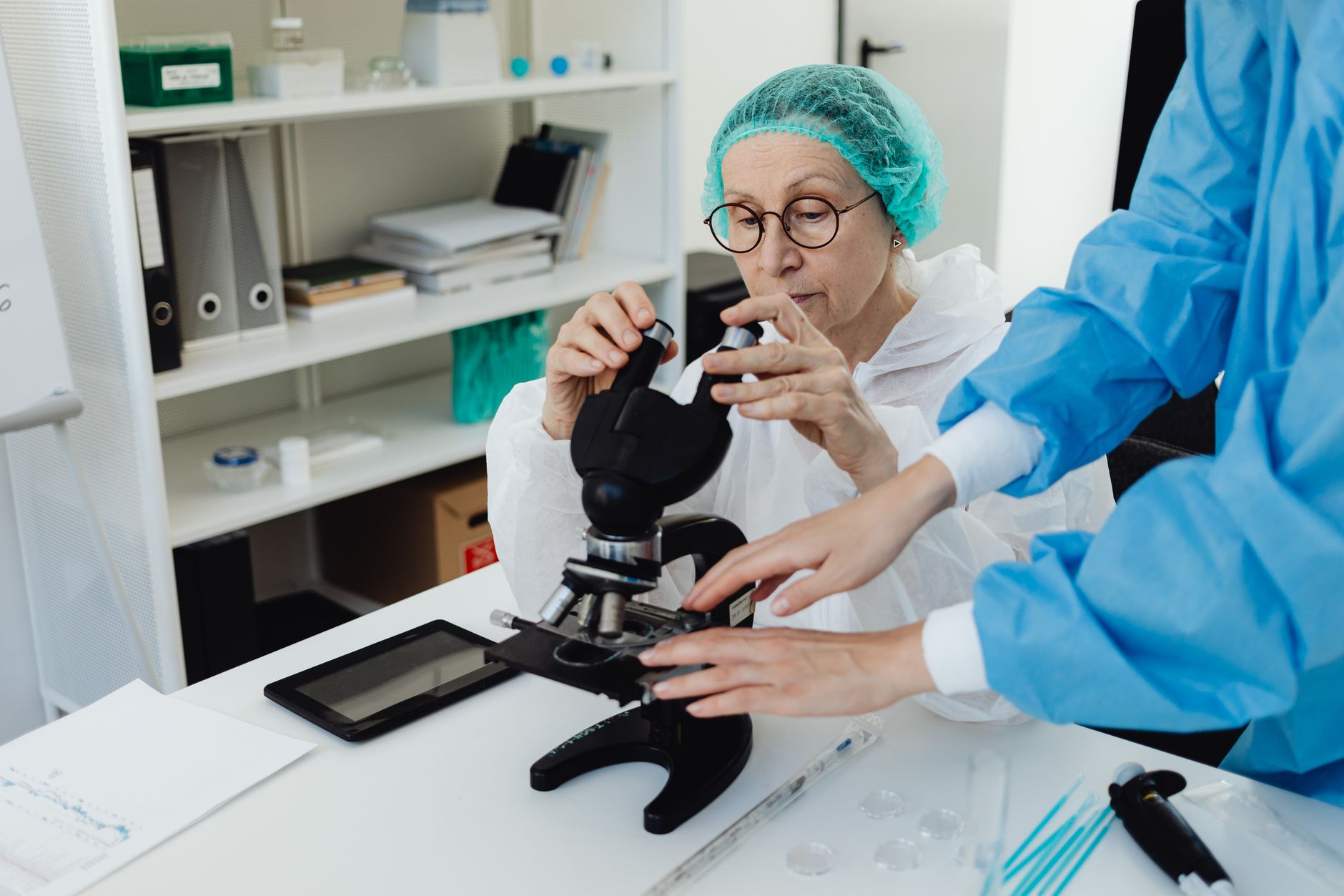 Senior researcher working with a microscope in a laboratory setting, assisted by