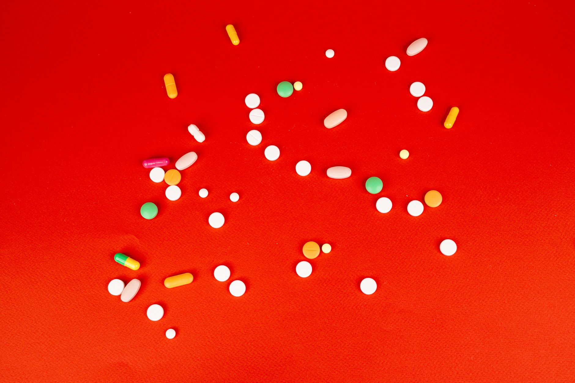 A colorful assortment of pills and capsules scattered on a bright red