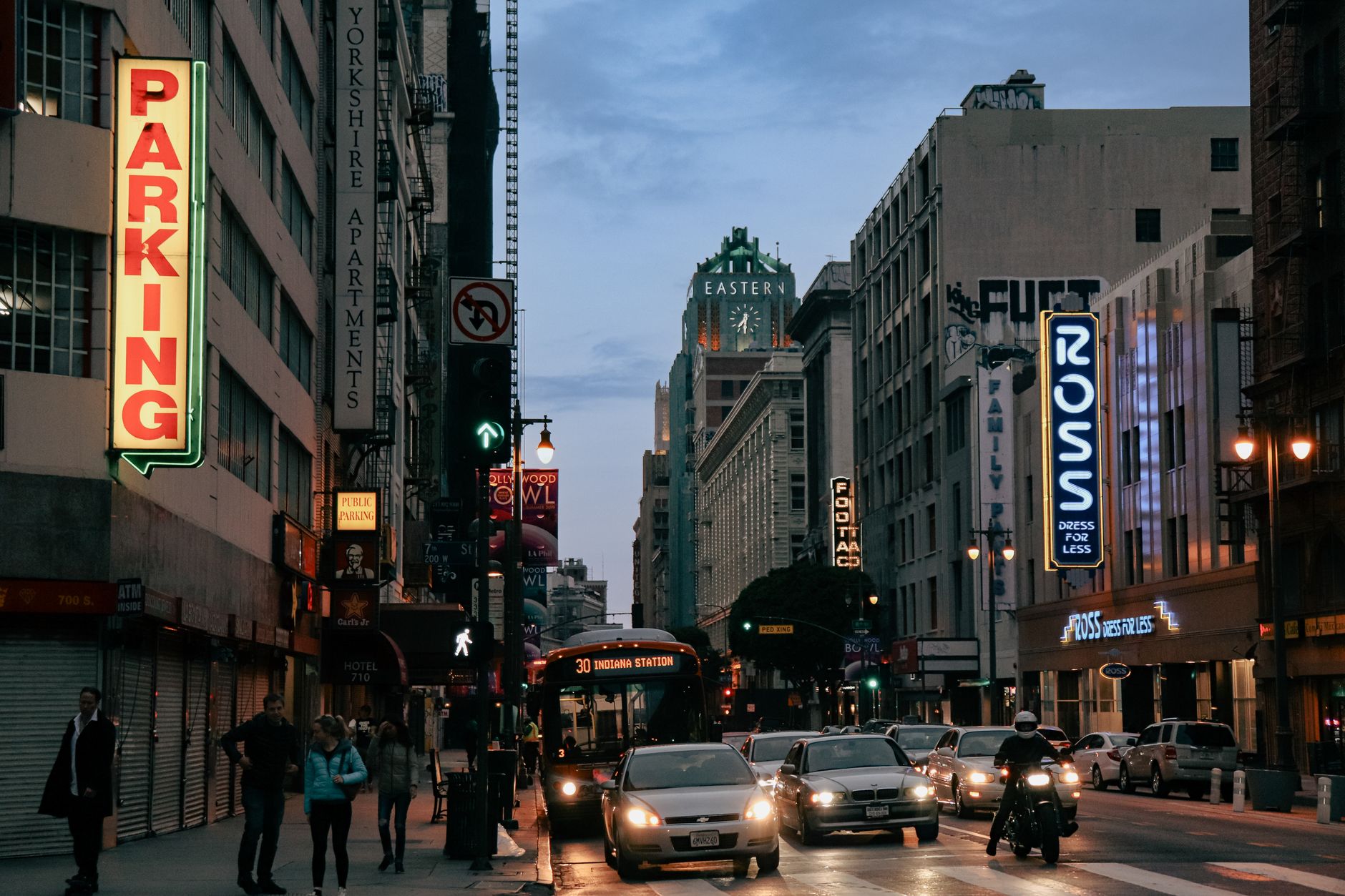City life in downtown Los Angeles with traffic and pedestrians at dusk.