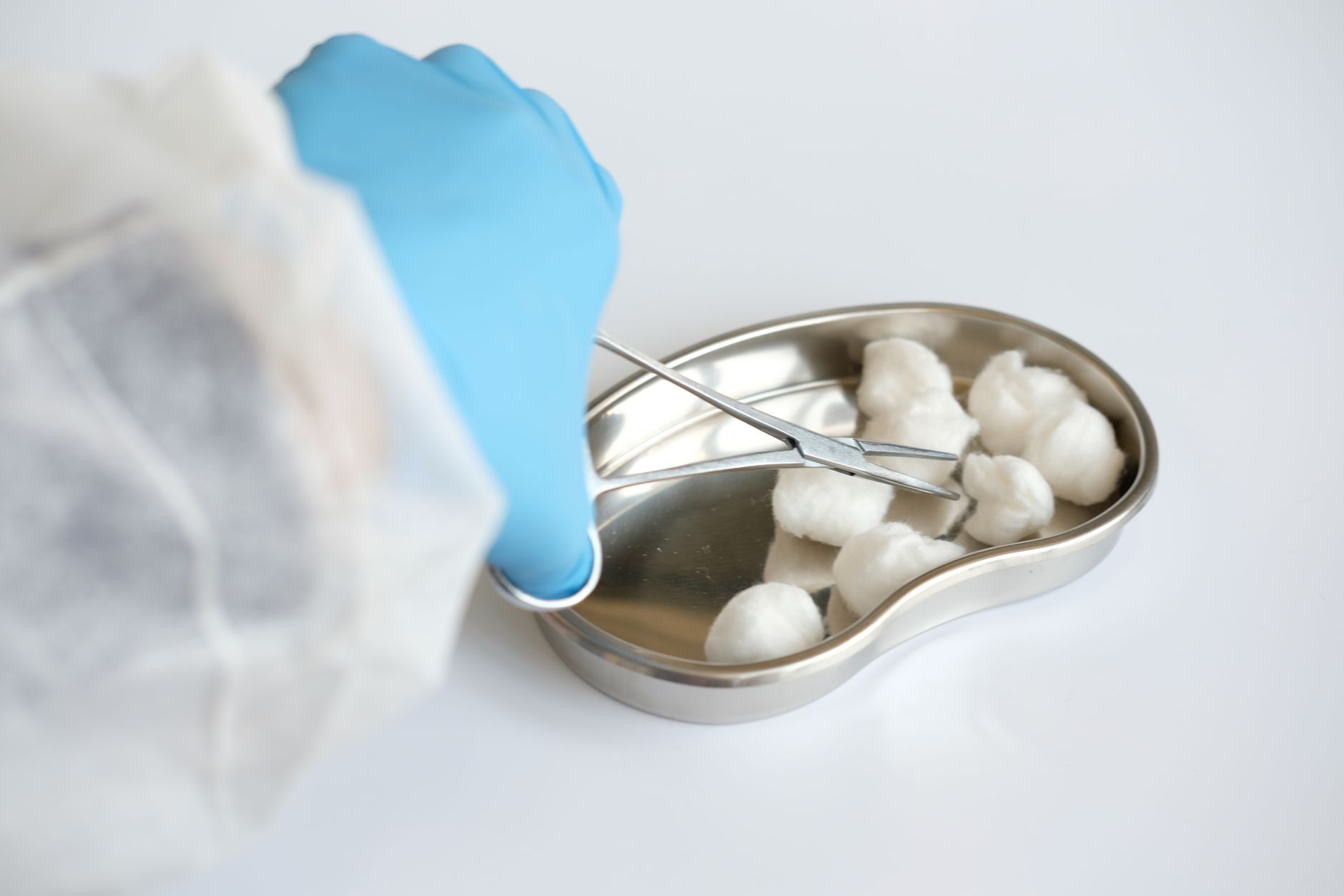 Close-up of latex gloved hand using forceps to handle cotton balls in