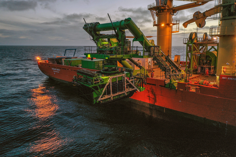 A large orange and green ship lowers the much smaller green Patania II vessel into the ocean.
