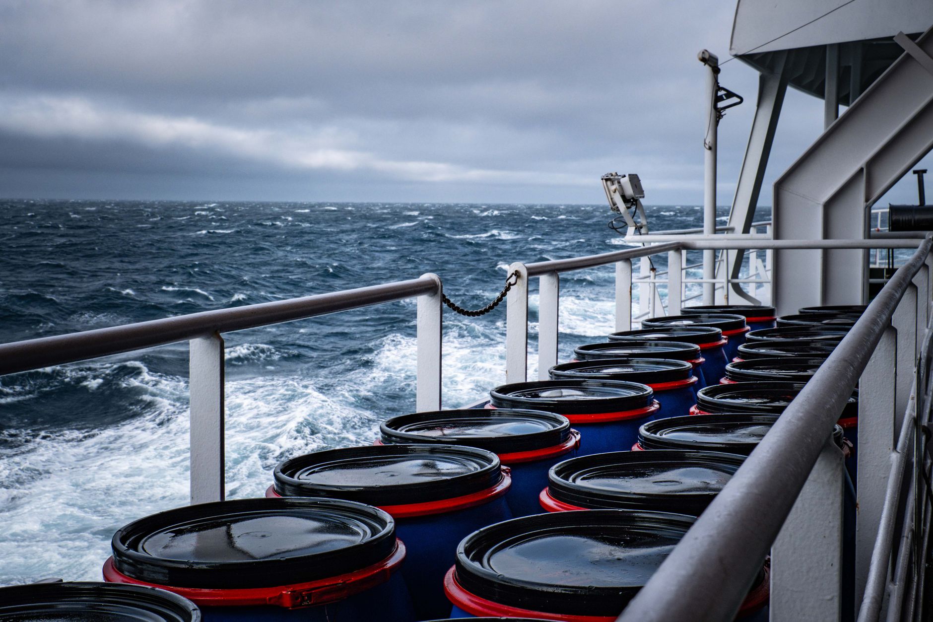 Industrial barrels stacked on a ship deck amidst a stormy sea, suggesting