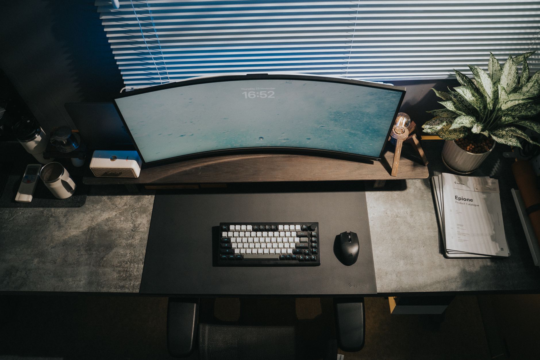 Stylish home office setup with a curved monitor, keyboard, and a lush