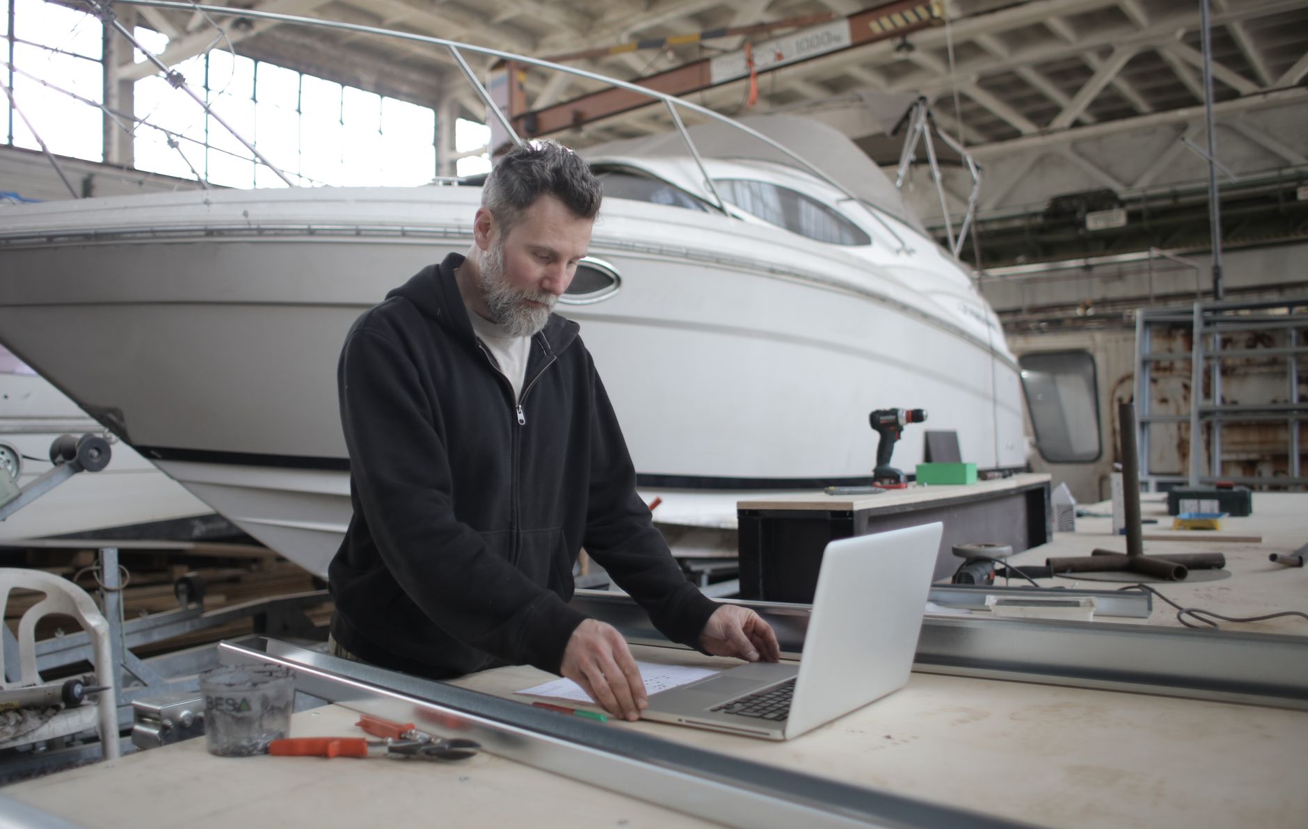 Concentrated adult bearded mechanic in casual outfit using laptop while working with