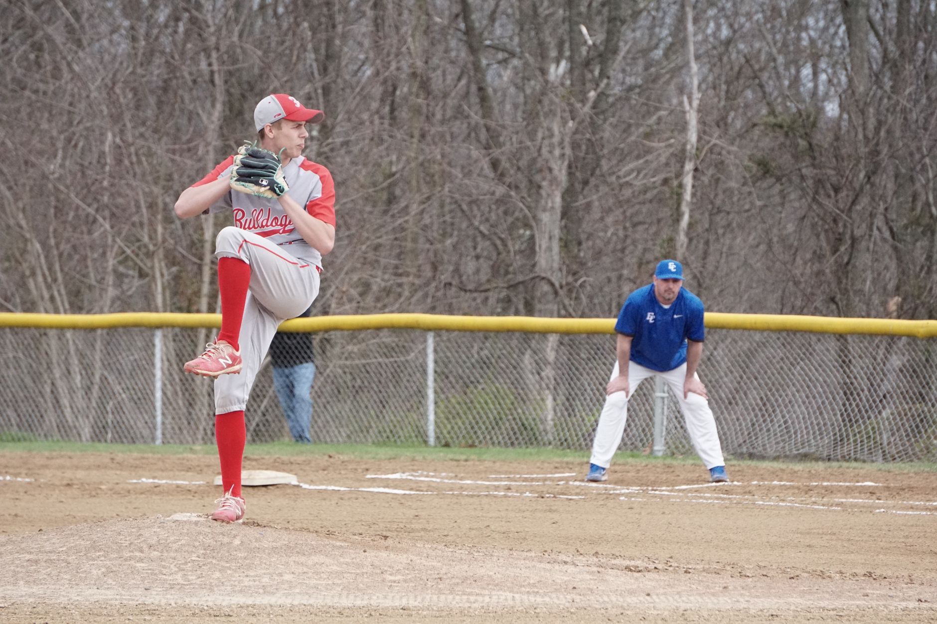 A high school baseball pitcher delivering a pitch during a game outdoors.