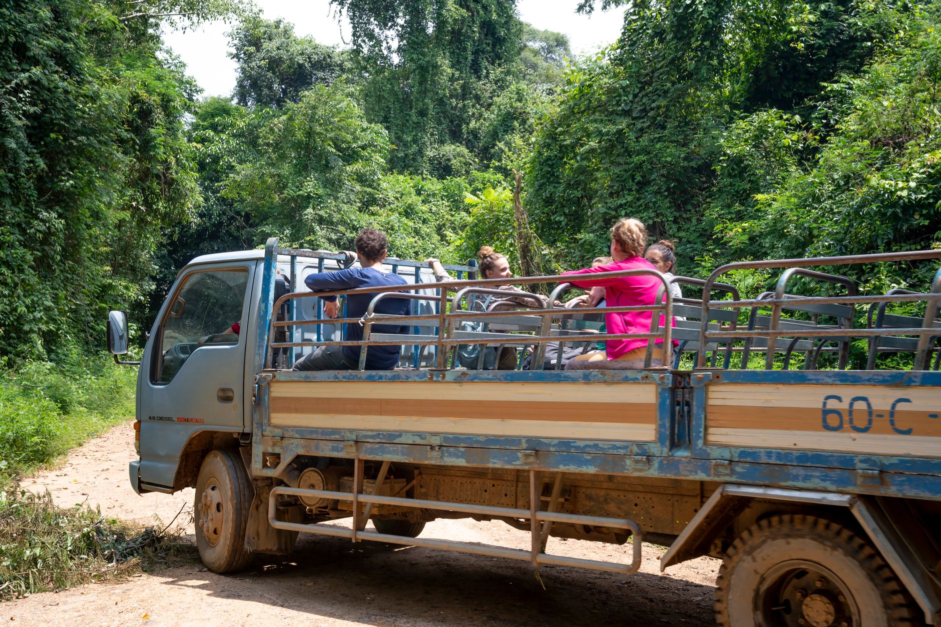 Travelers sitting in truck driving on dusty road in lush forest while