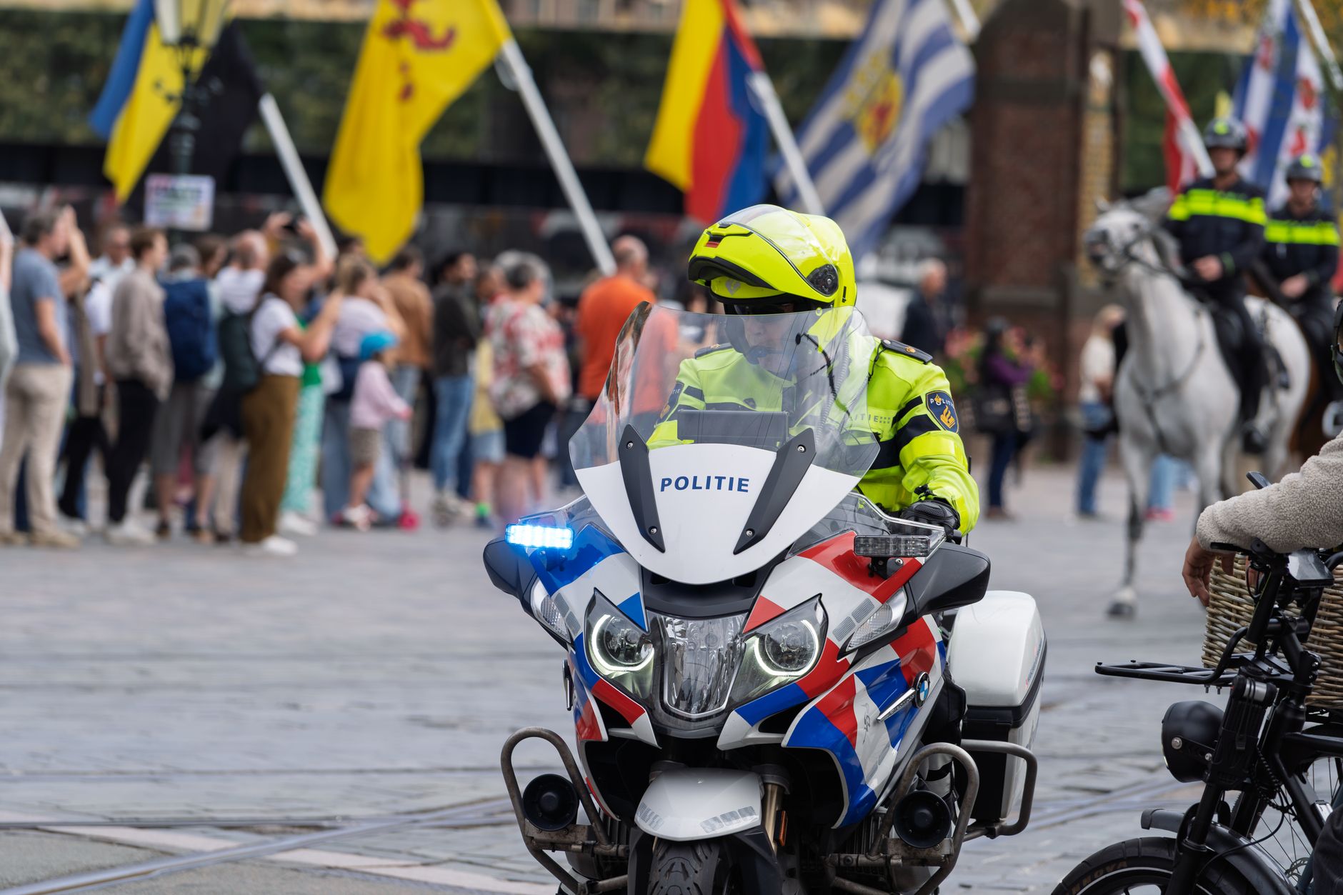 Dutch police officer on a decorated motorcycle managing crowd at outdoor event.