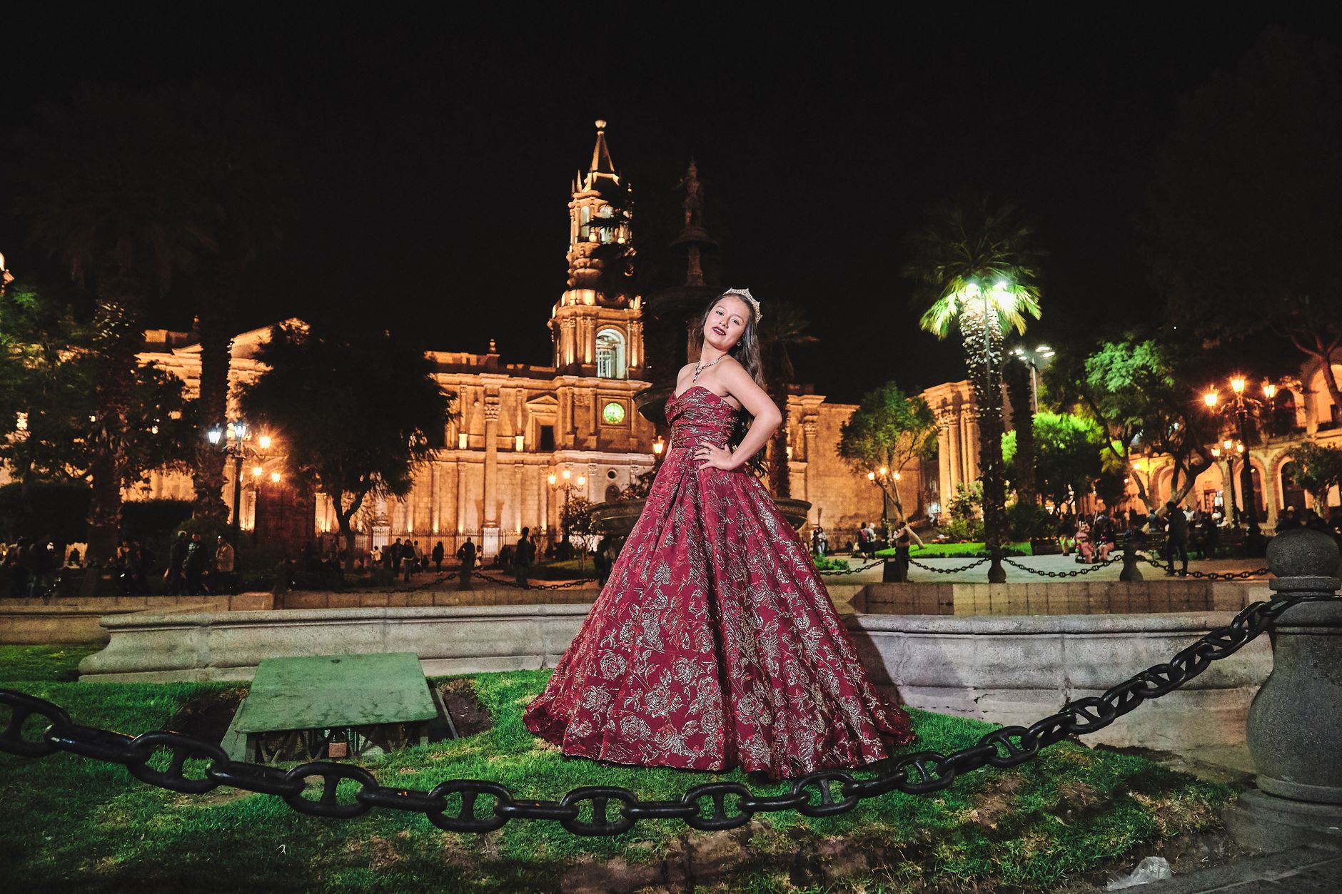 Woman posing in a floral evening gown at a night-lit historic plaza