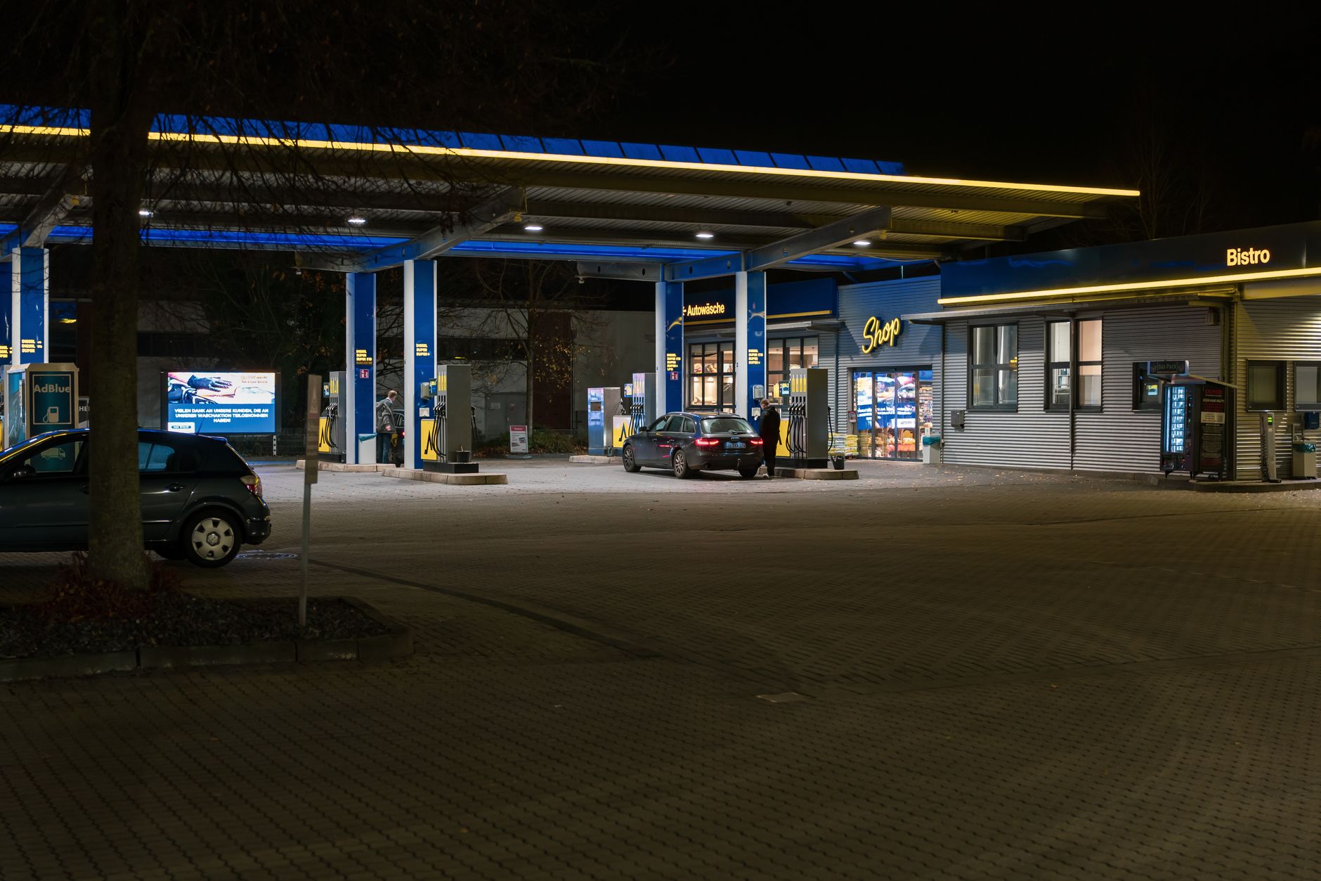 A well-lit gas station at night featuring cars and a bistro, creating