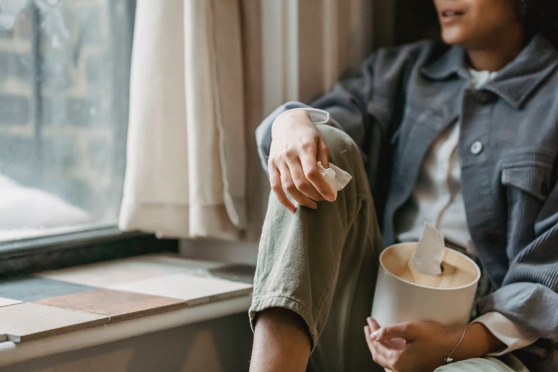 Crop unrecognizable upset ethnic female millennial in casual outfit sitting near window