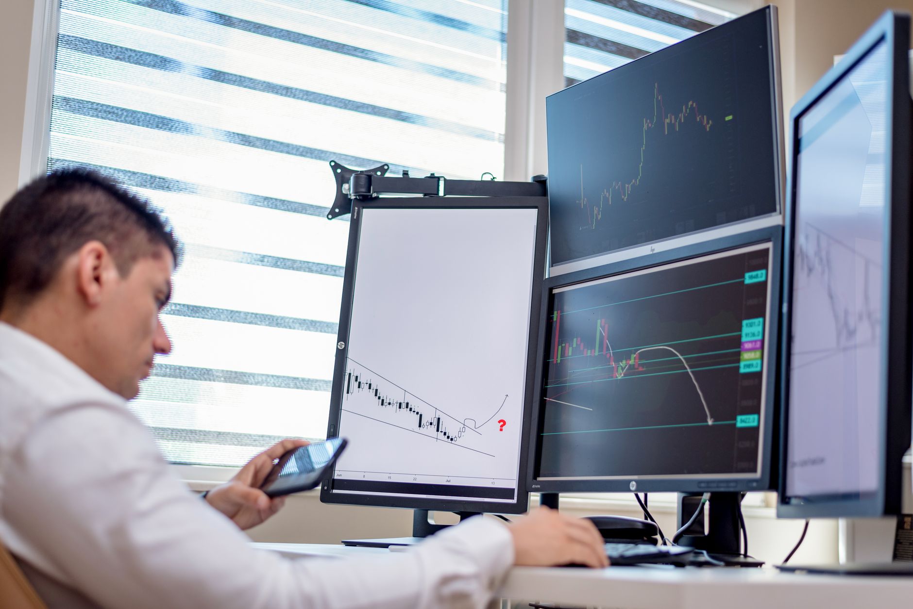 A stock trader analyzes financial data on multiple computer screens in an