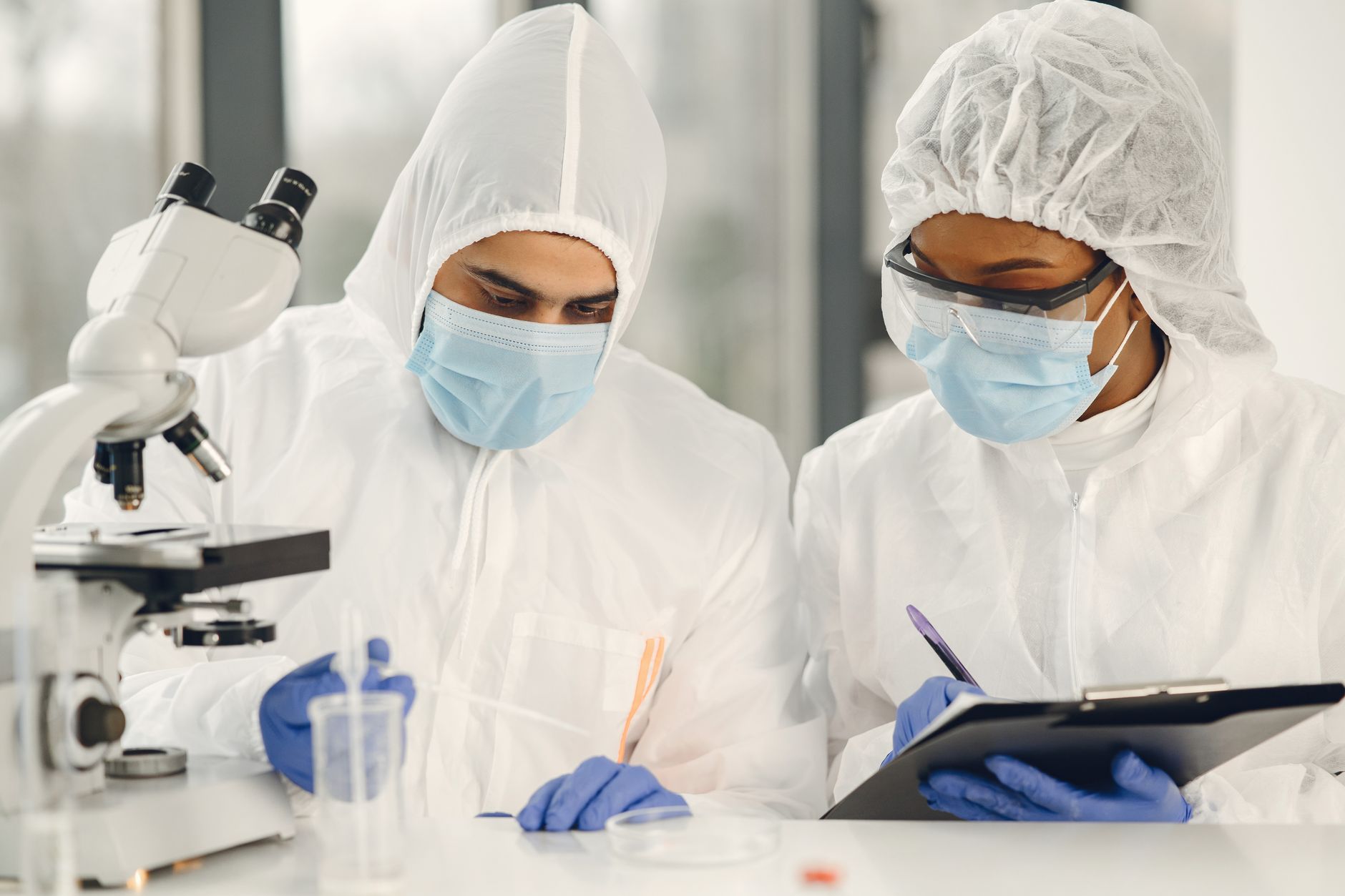 Two scientists in hazmat suits working with a microscope and notes in